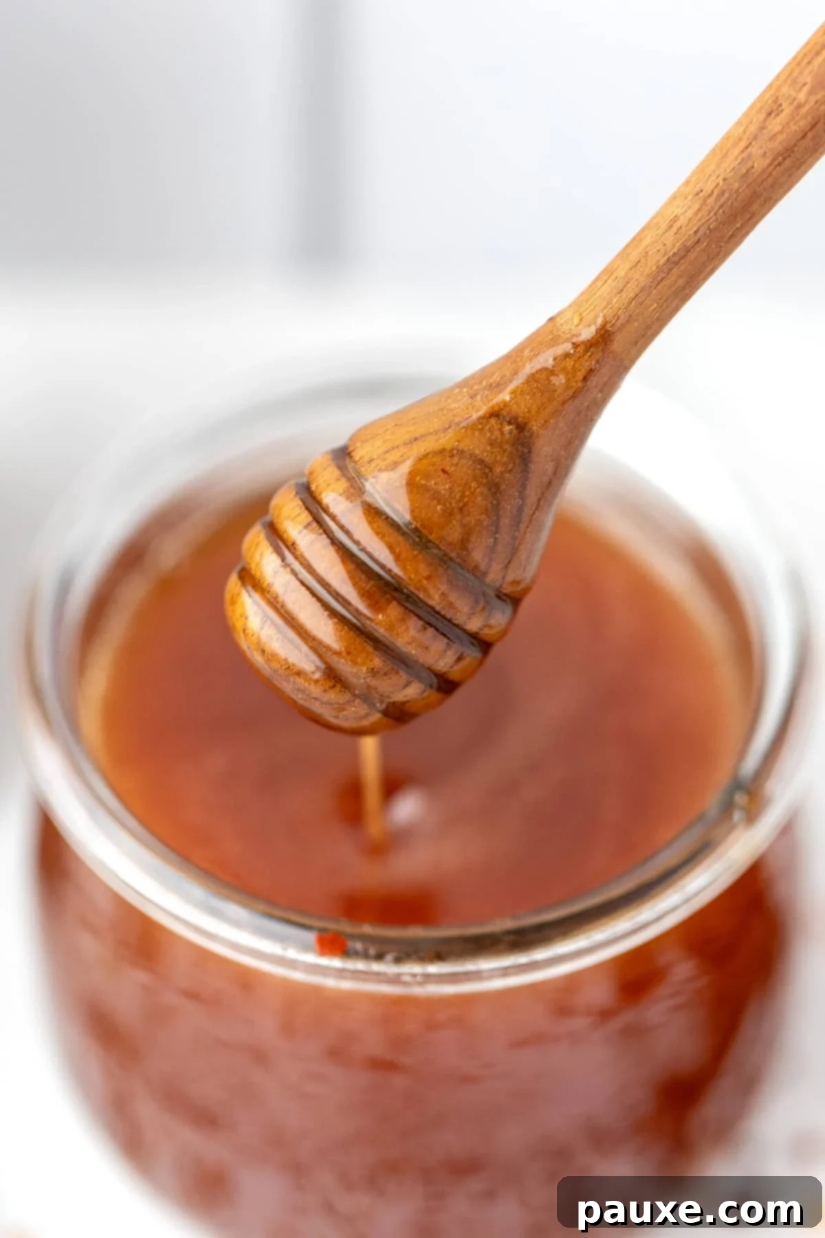 Crafting Homemade Hot Honey 10 A honey dipper taking a generous amount of hot honey from a jar, showcasing its beautiful texture.