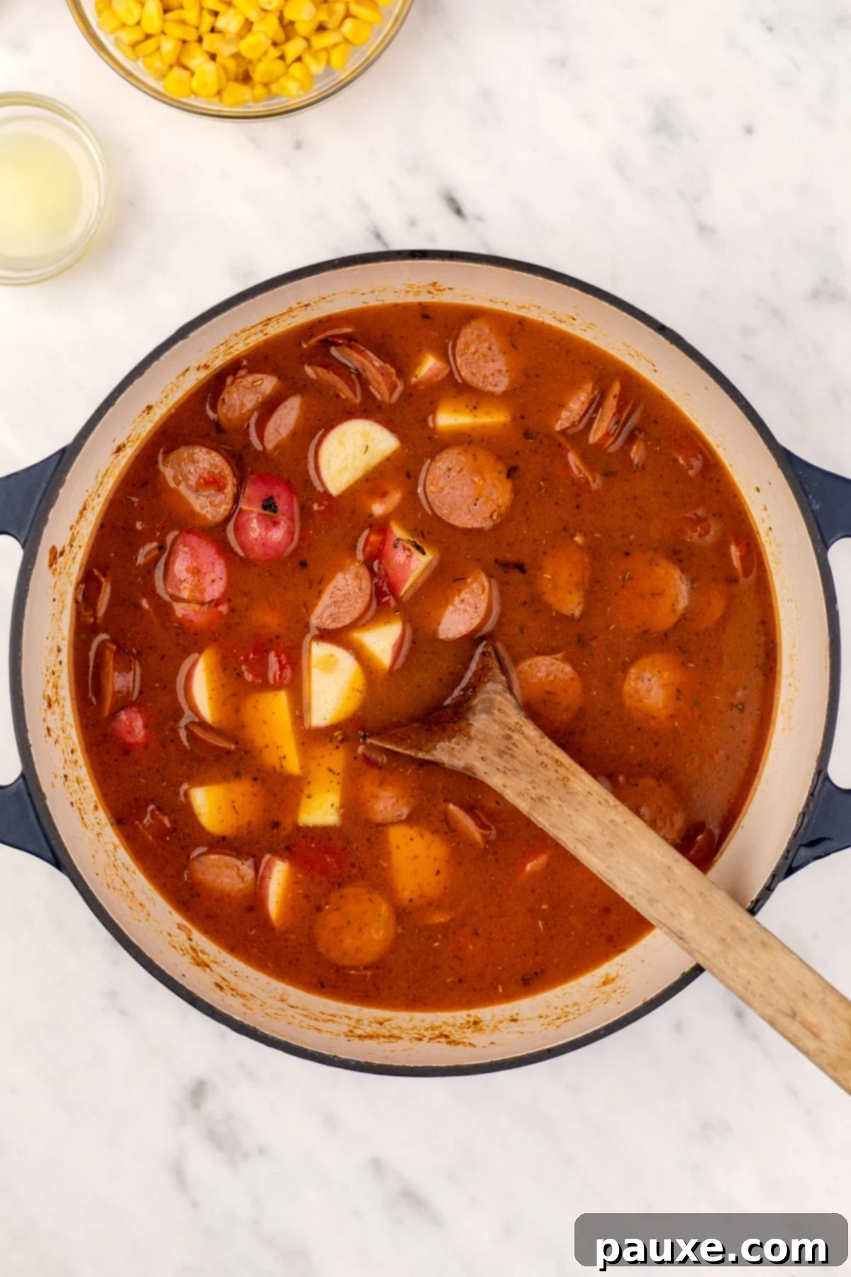 Mossy Potage 6 A Dutch oven simmering with Swamp Soup, showing tender chunks of potato and sliced smoked sausage submerged in the flavorful broth.