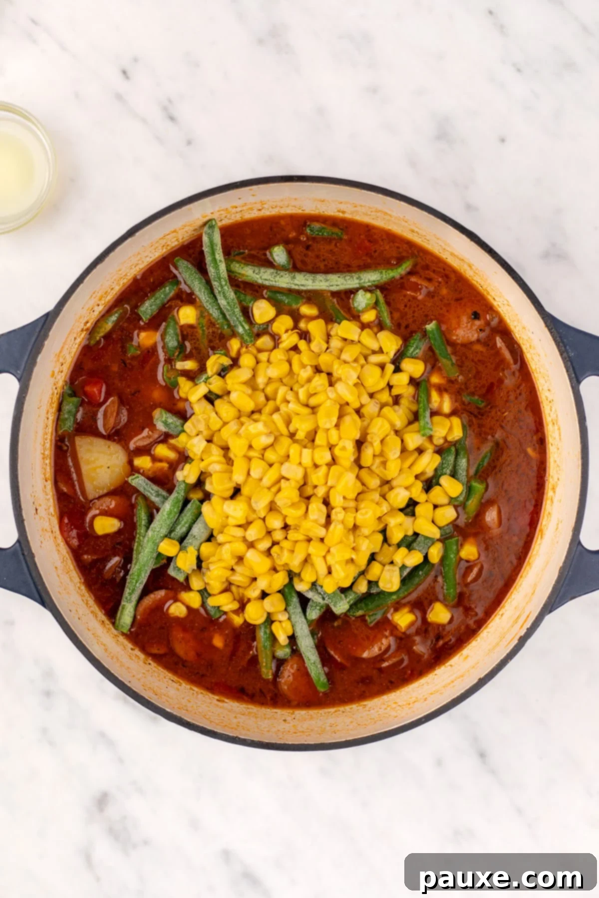 Mossy Potage 7 Frozen green beans and corn being added to a large Dutch oven full of simmering Swamp Soup.