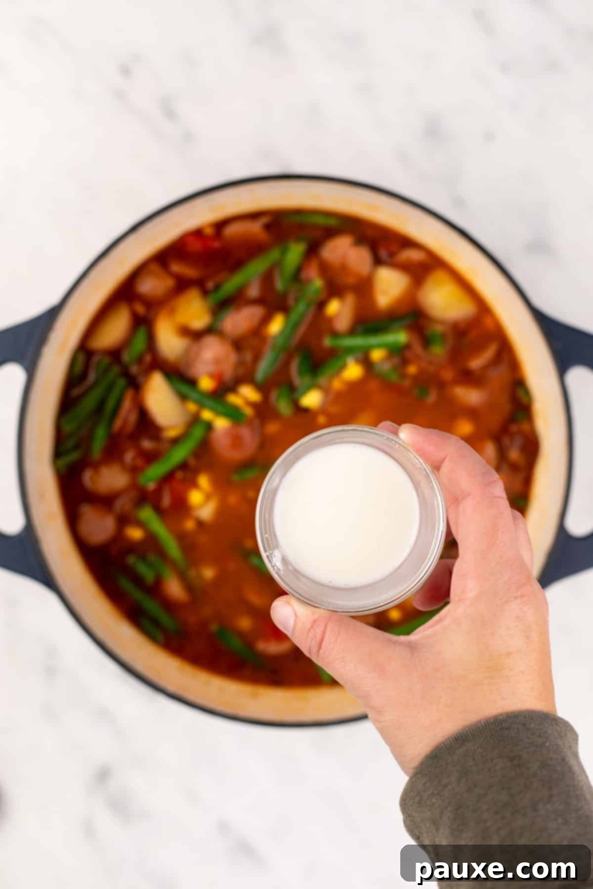 Mossy Potage 8 A small bowl of cornstarch slurry held above a large pot of Swamp Soup, ready to be added for thickening.