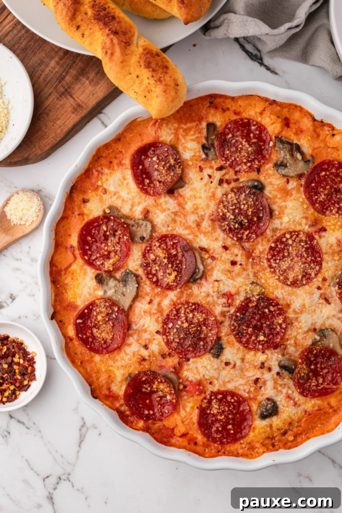 Baked Pepperoni Pizza Dip 2 A bubbly baked pepperoni pizza dip, topped with melted cheese and pepperoni slices, surrounded by golden-brown breadsticks ready for dipping.