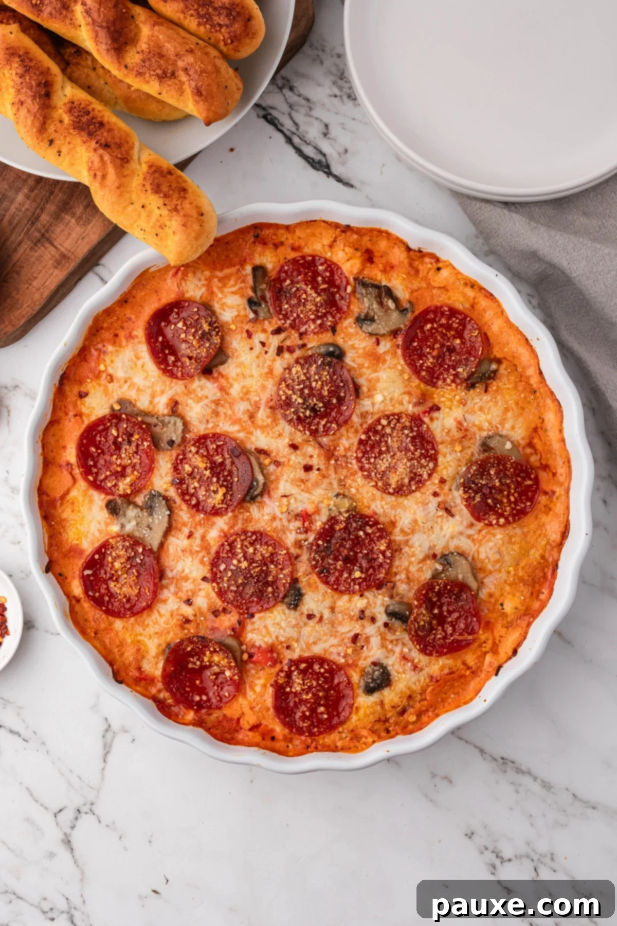 Baked Pepperoni Pizza Dip 8 Bubbly and hot pizza dip in a round white baking dish, garnished with fresh basil, with golden garlic breadsticks on the side ready for dipping.