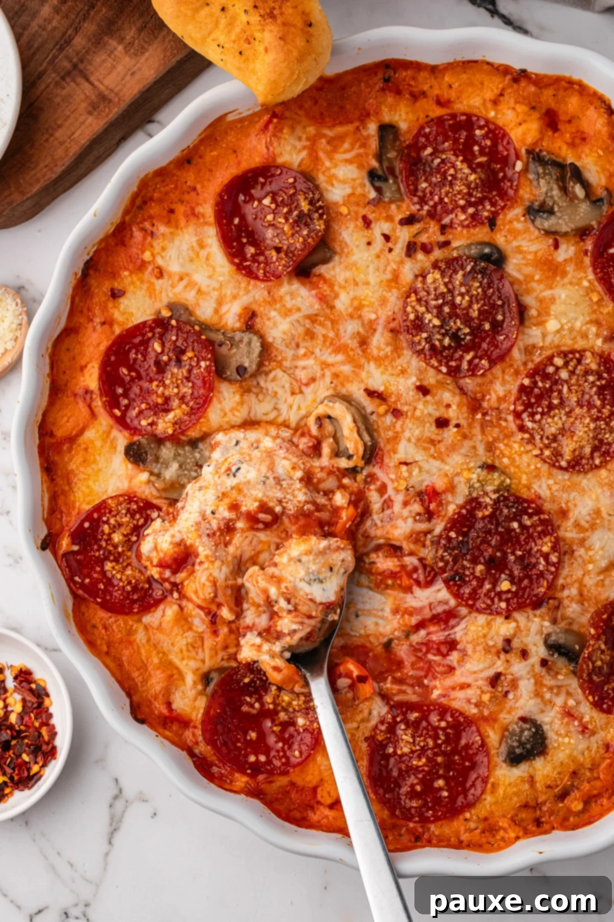 Baked Pepperoni Pizza Dip 10 A spoon scooping creamy, melted cheese and sauce from a round baking dish, showing the rich layers of the pizza dip.