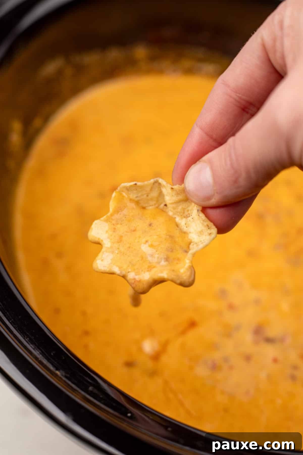 A tortilla chip being dipped into a slow cooker full of creamy, cheesy Rotel dip with ground beef.