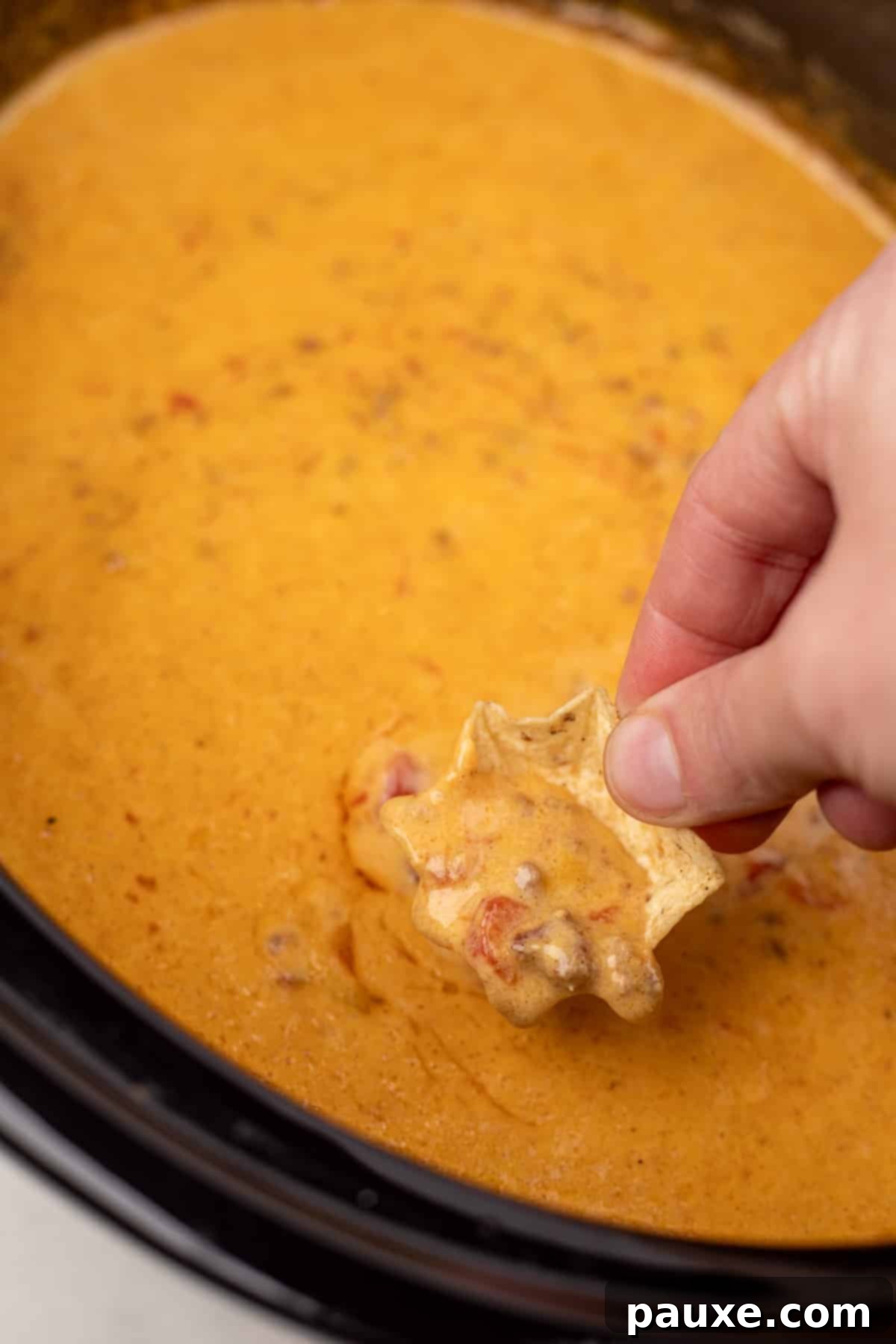 Dipping a tortilla chip into a slow cooker filled with warm, cheesy Rotel dip.