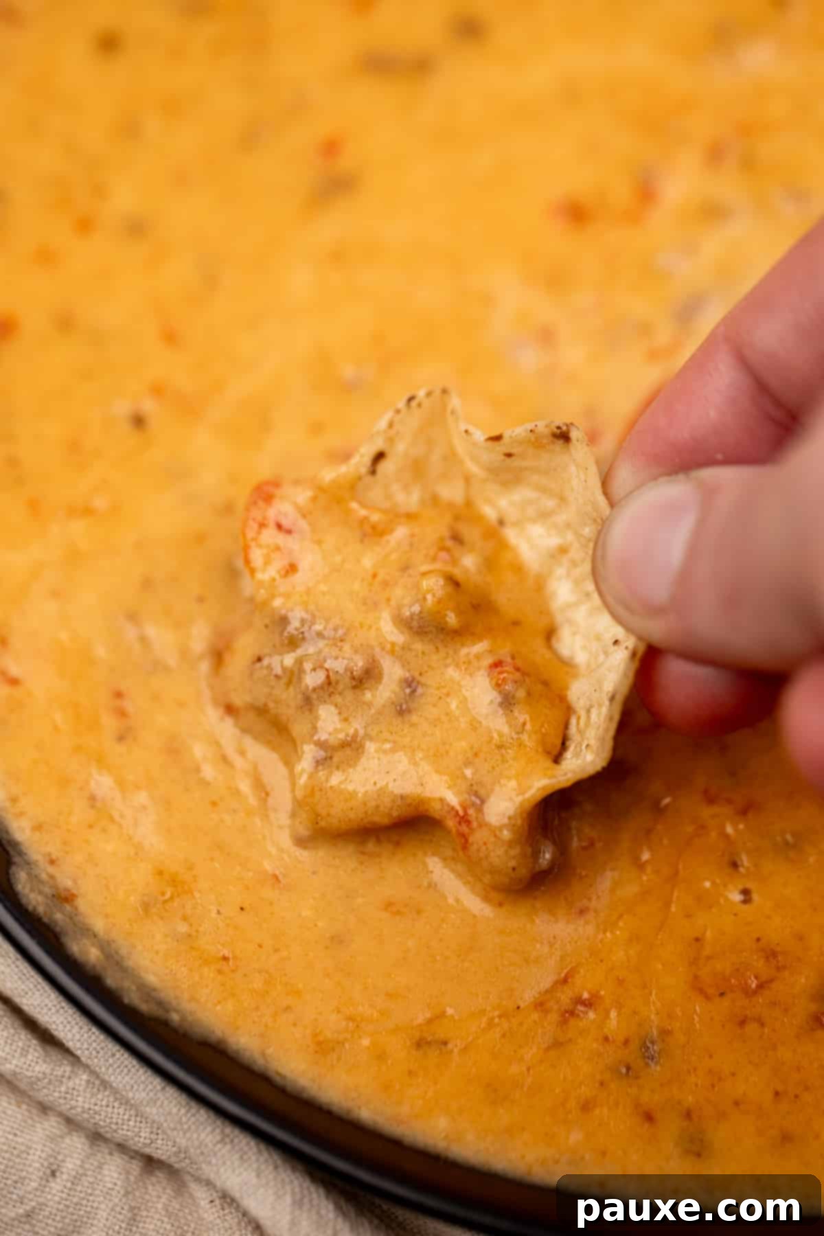 Dipping a tortilla chip into a hearty, cheesy ground beef dip, ready for a party.