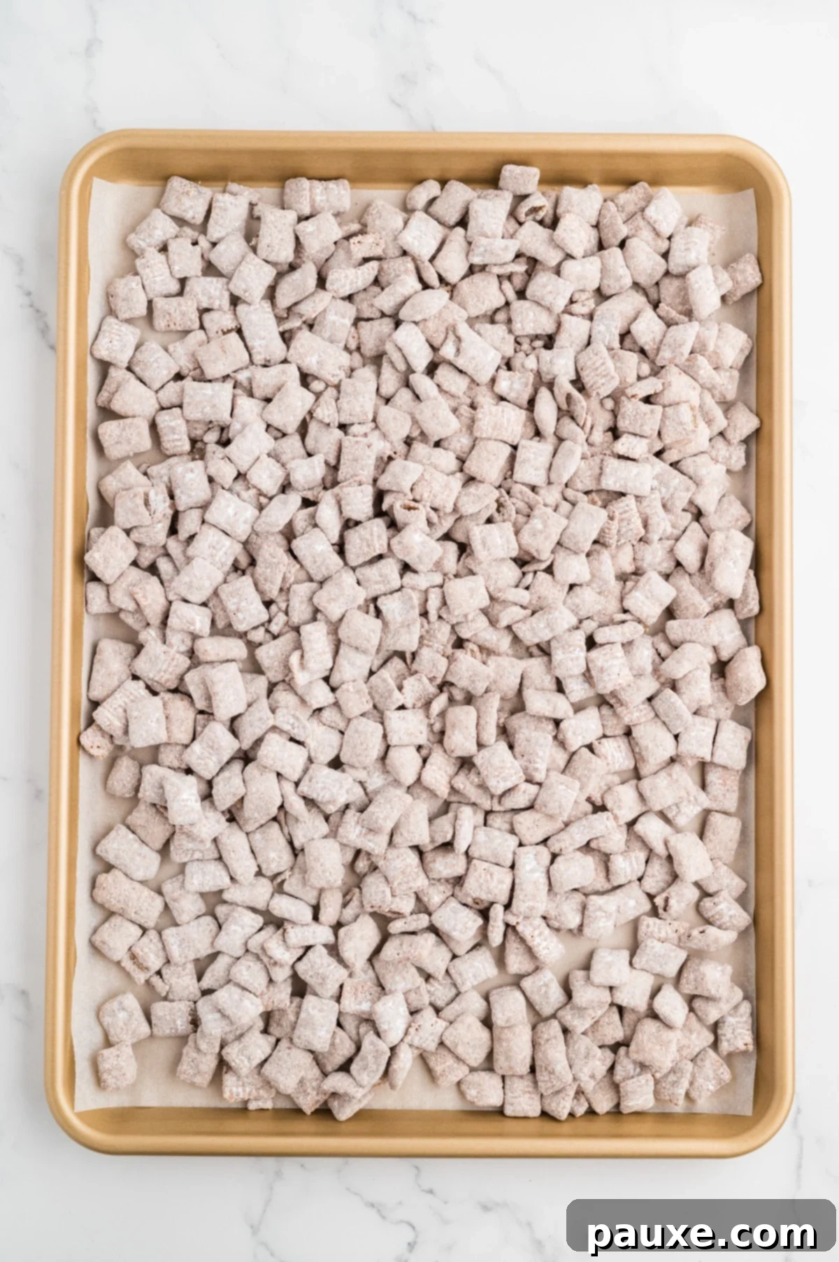 A sheet pan filled with homemade muddy buddies snack mix.