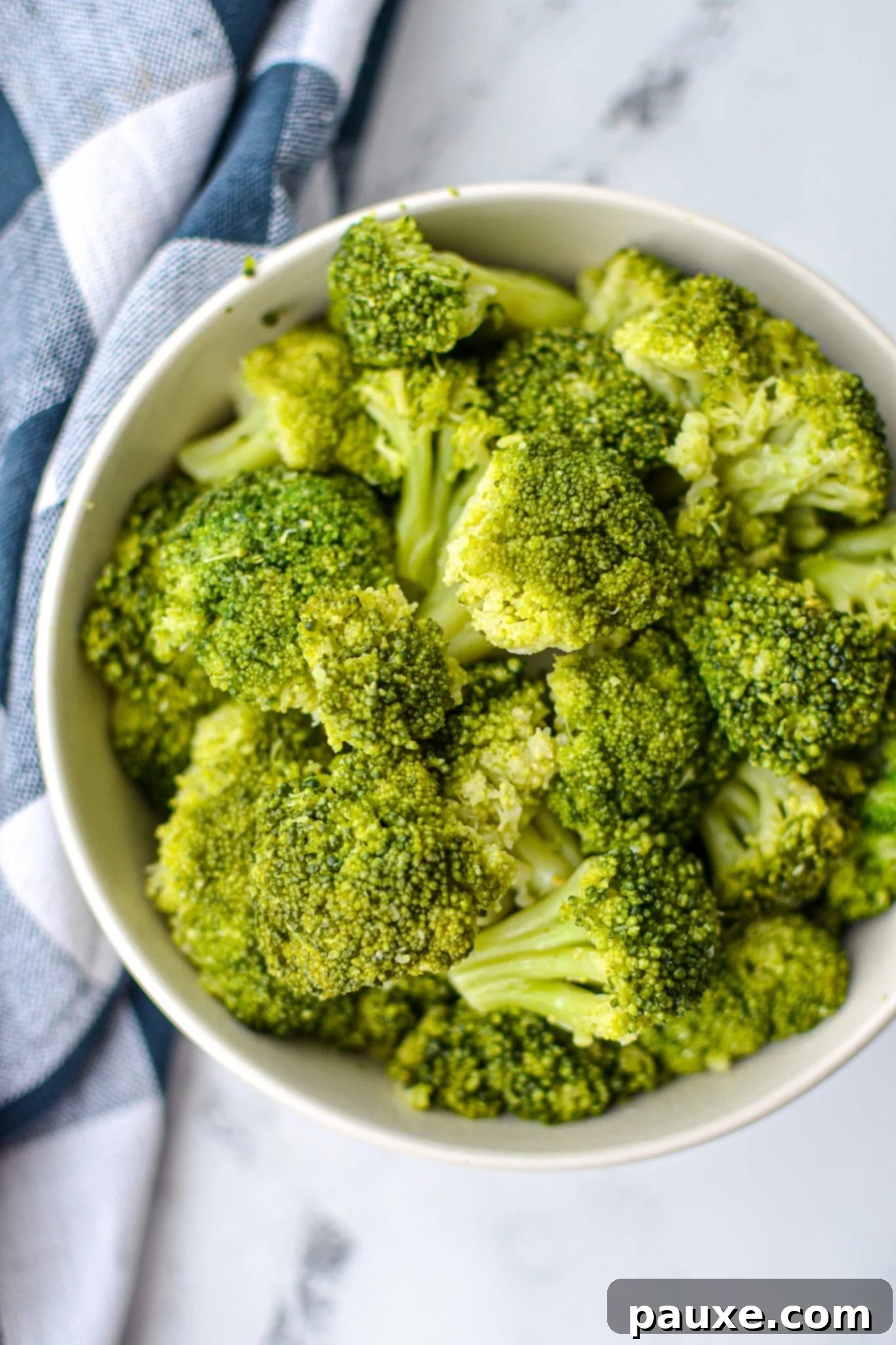 Perfect Instant Pot Frozen Broccoli 3 An overhead shot of a bowl of cooked broccoli, resting on a white marble counter and with a blue check napkin, ready to be served.