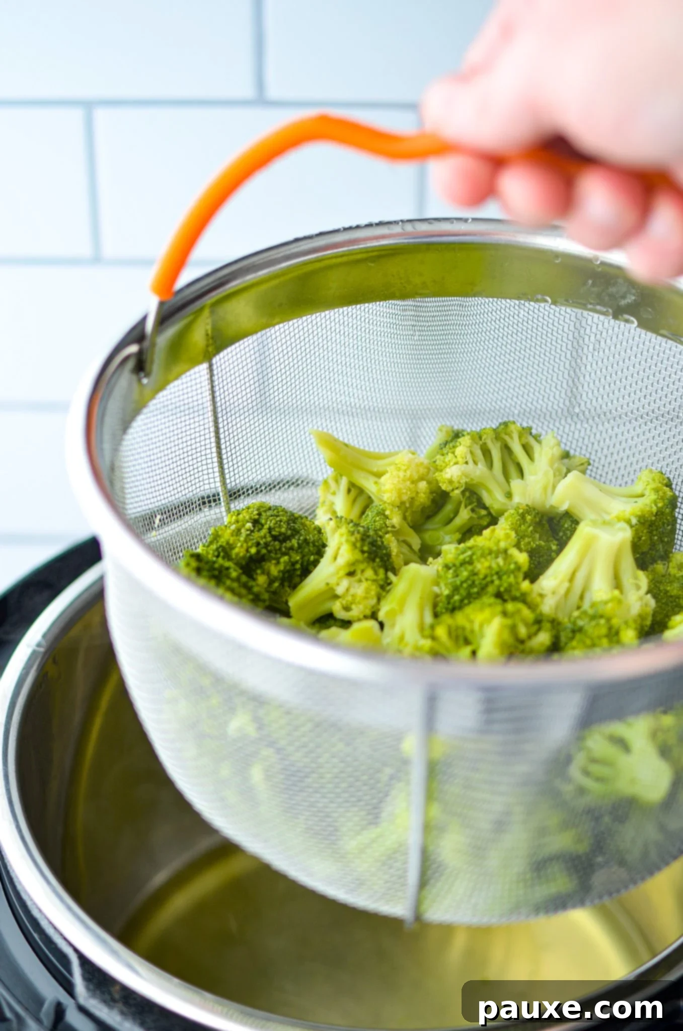 Perfect Instant Pot Frozen Broccoli 10 Lifting the steamer basket out of the Instant Pot with cooked broccoli inside, ready to be drained and served.