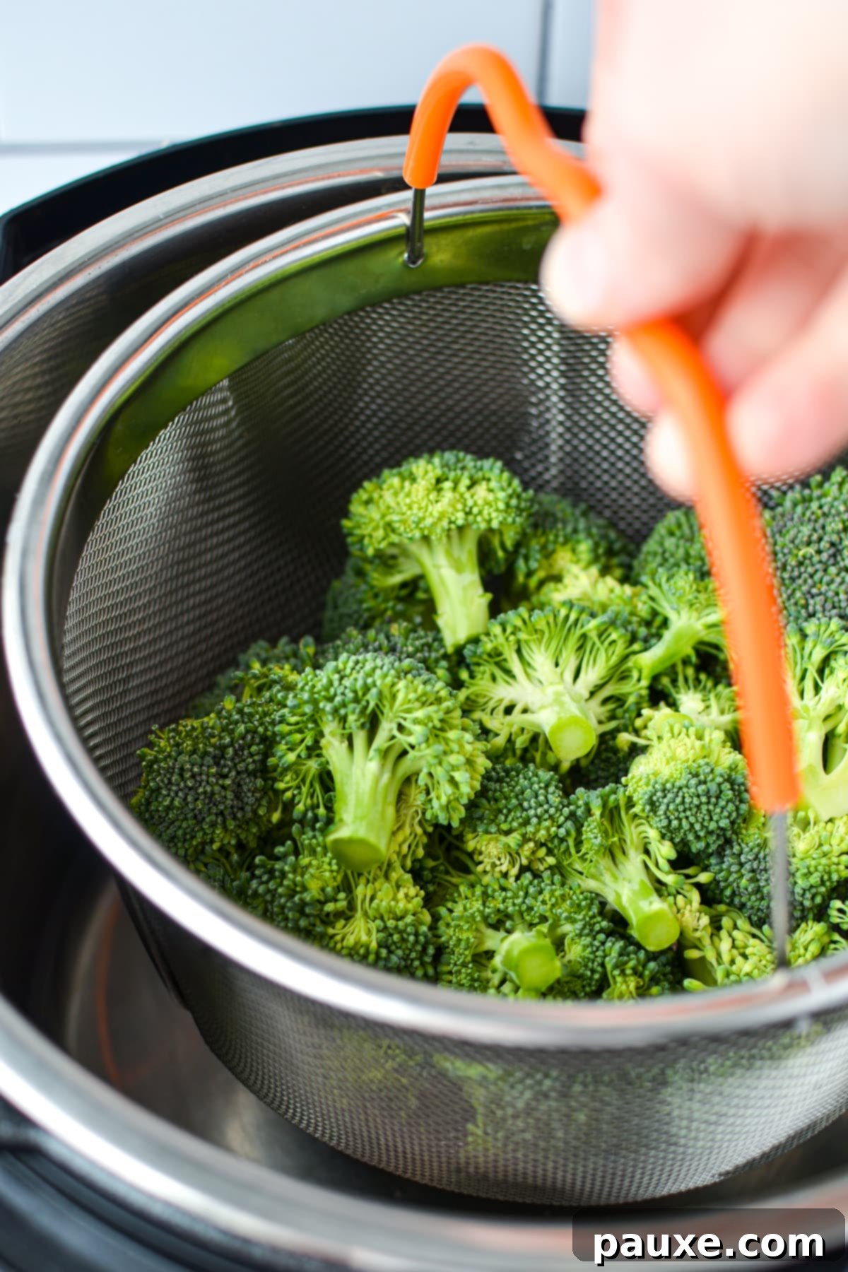 Effortless Instant Pot Broccoli 4 A person is carefully lowering a metal steamer basket filled with fresh broccoli florets into the inner pot of an Instant Pot.