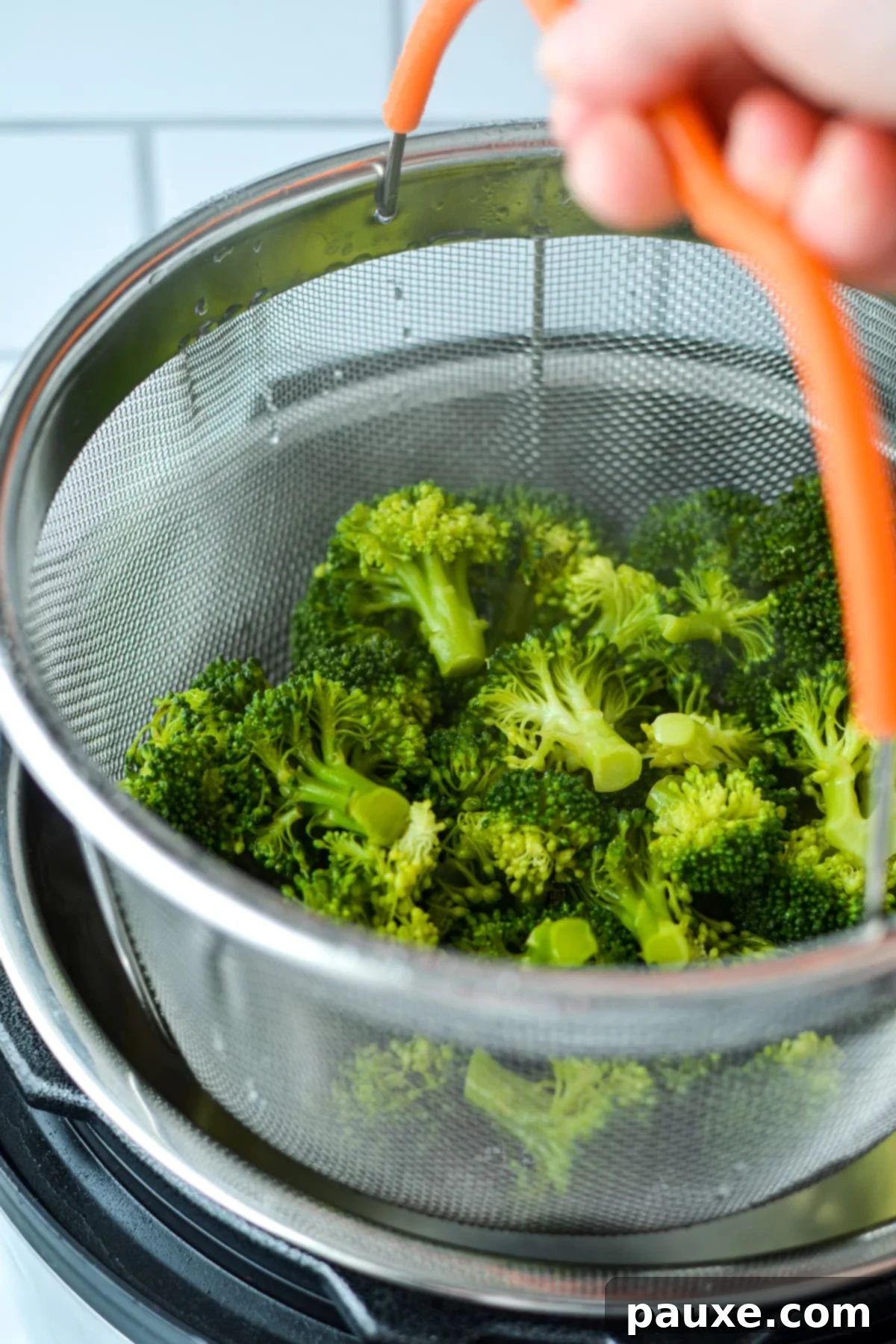 Effortless Instant Pot Broccoli 5 A hand wearing an oven mitt is carefully lifting a steamer basket overflowing with bright green, perfectly cooked broccoli from an Instant Pot.