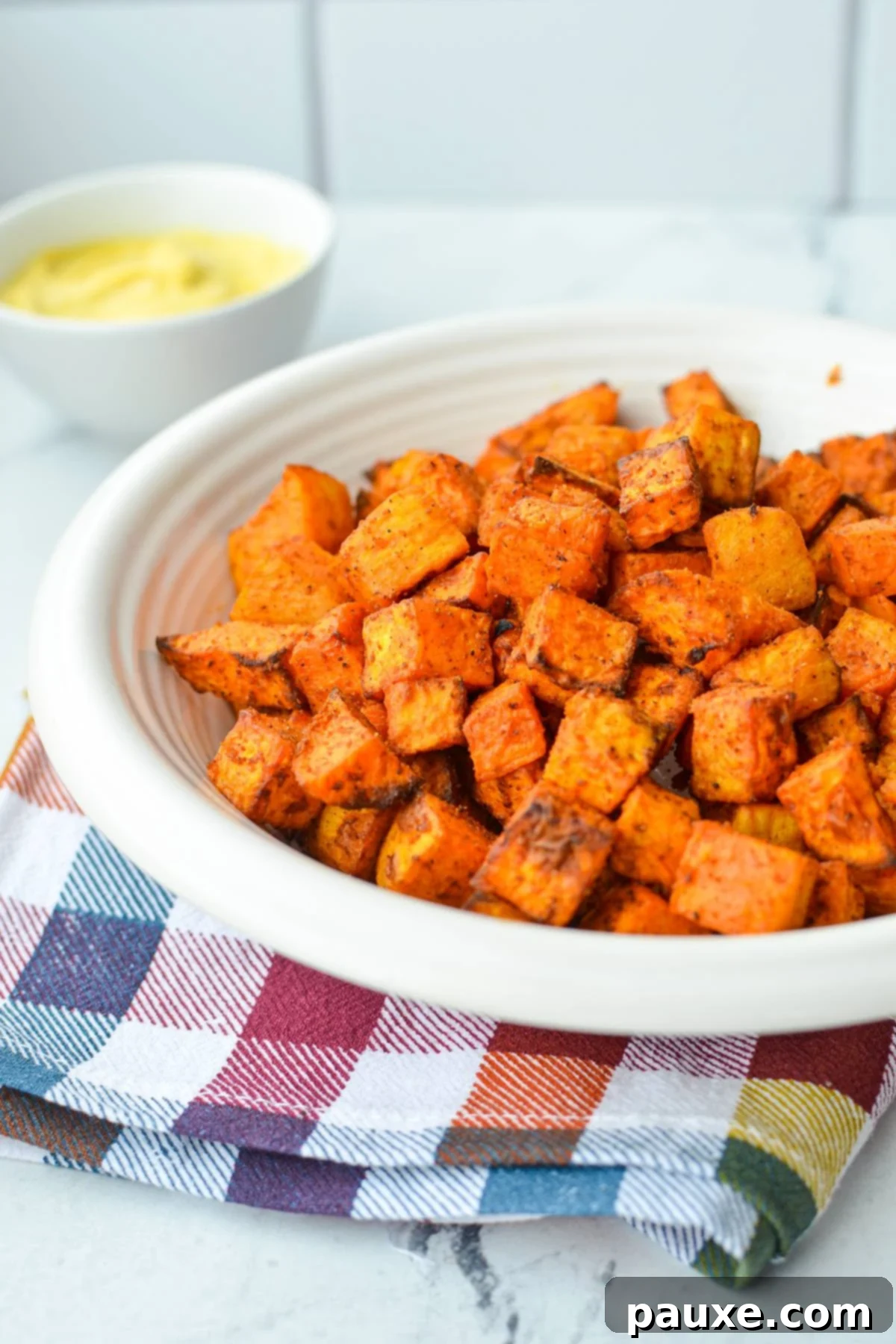 Crispy Air Fryer Sweet Potato Cubes 8 A beautifully presented bowl of roasted sweet potato cubes, with a small dish of creamy dipping sauce blurred in the background.