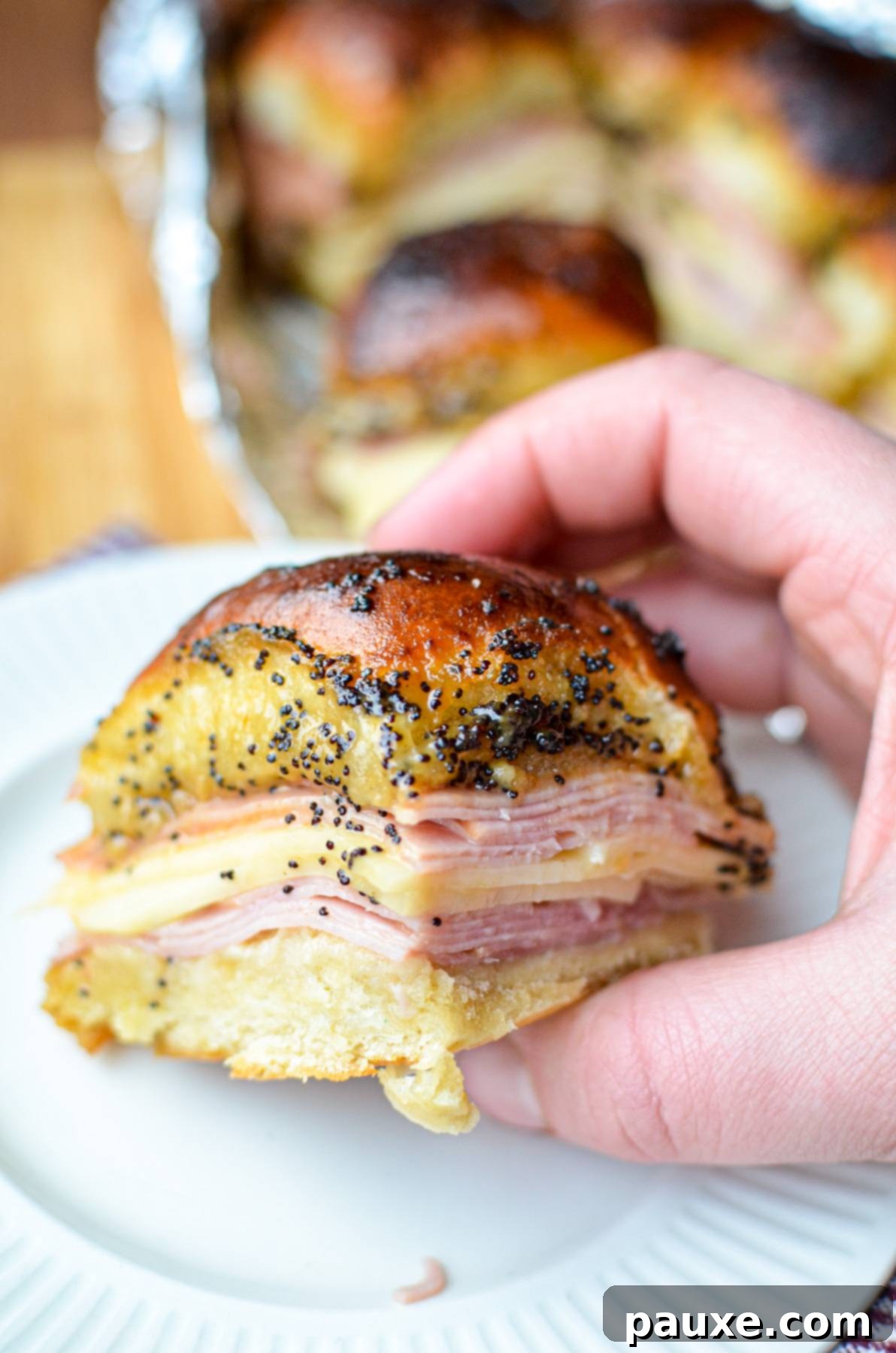 Golden Air Fryer Ham and Cheese Sliders 2 Holding a ham and cheese slider, covered with a poppy seed sauce.