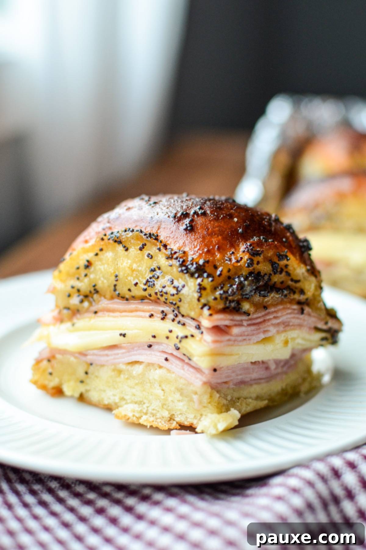 Golden Air Fryer Ham and Cheese Sliders 7 A single ham and cheese slider on a plate, covered in a poppy seed sauce.