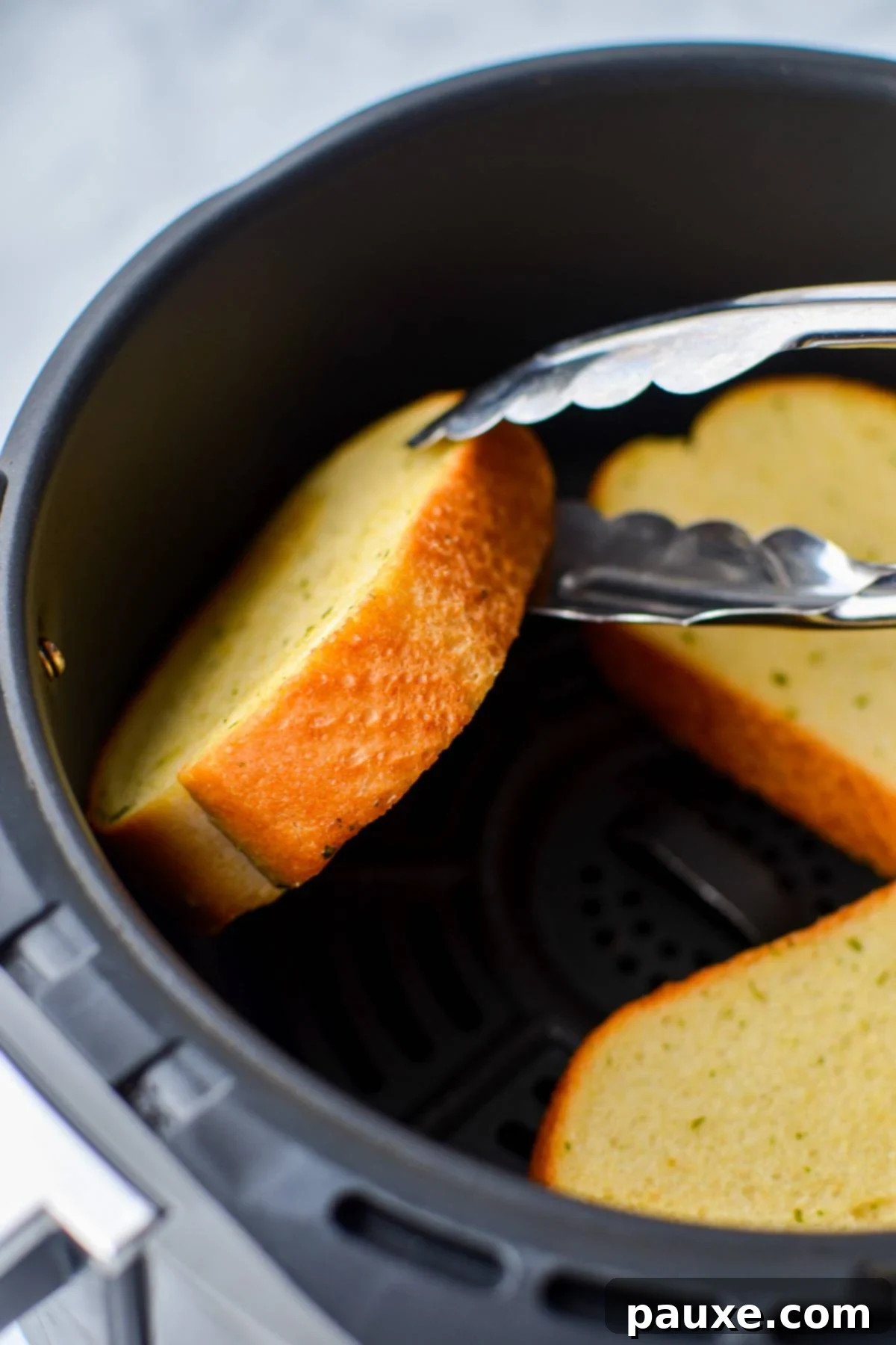 Crispy Air Fryer Texas Garlic Toast 6 A pair of tongs carefully flipping a slice of Texas Toast in an air fryer basket, ensuring even cooking.