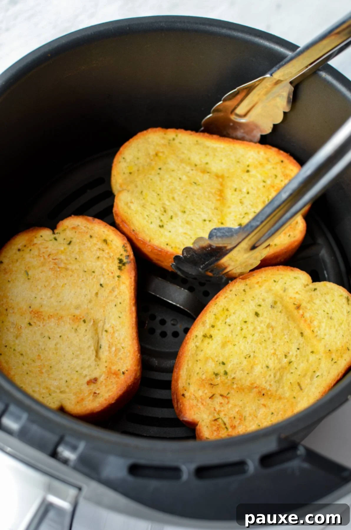 Crispy Air Fryer Texas Garlic Toast 8 Tongs lifting a slice of perfectly toasted frozen garlic bread from the cooking basket.