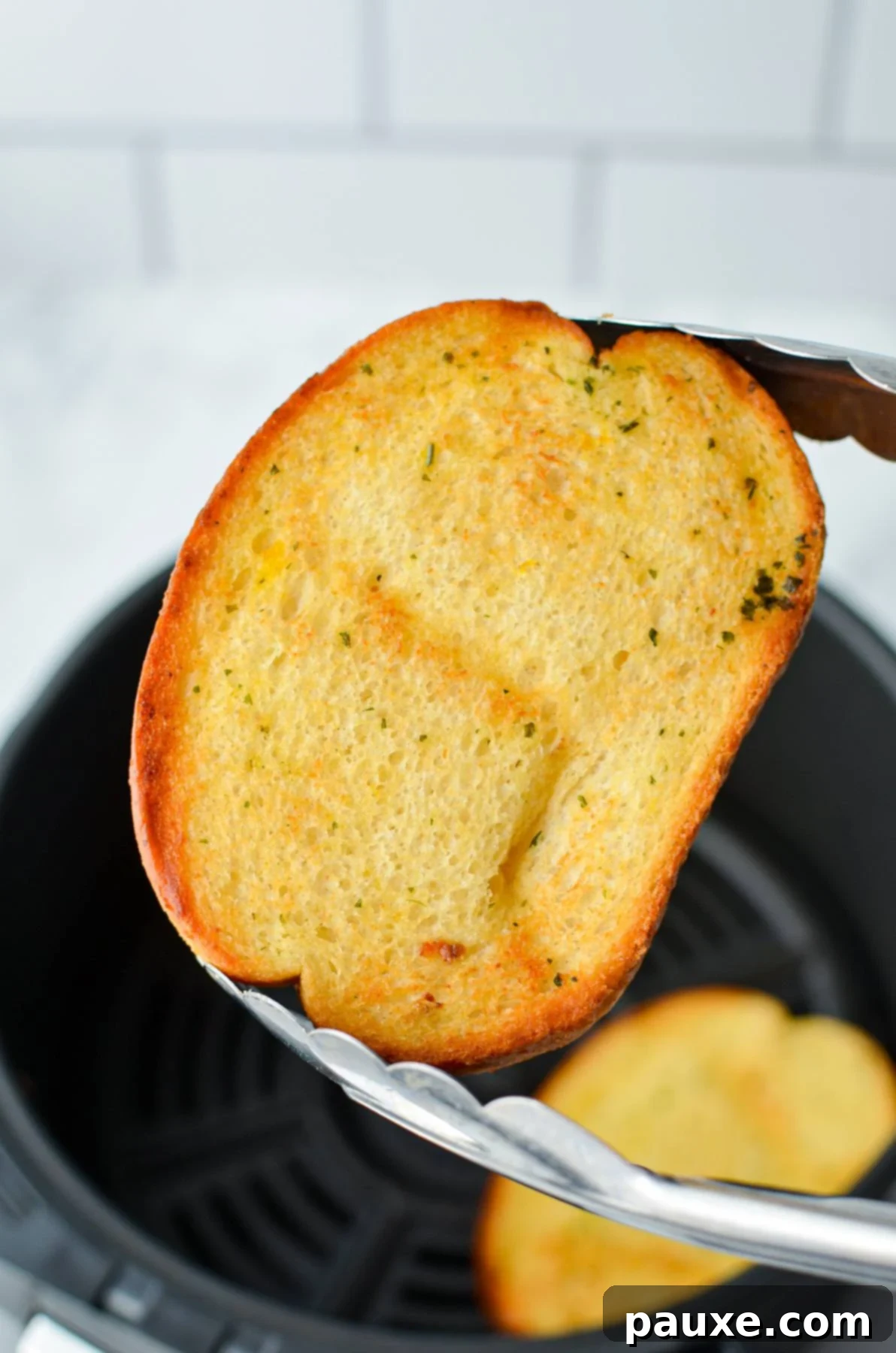 Crispy Air Fryer Texas Garlic Toast 9 A pair of tongs holding up a golden-brown, toasted piece of frozen garlic bread, showing off its crisp texture.
