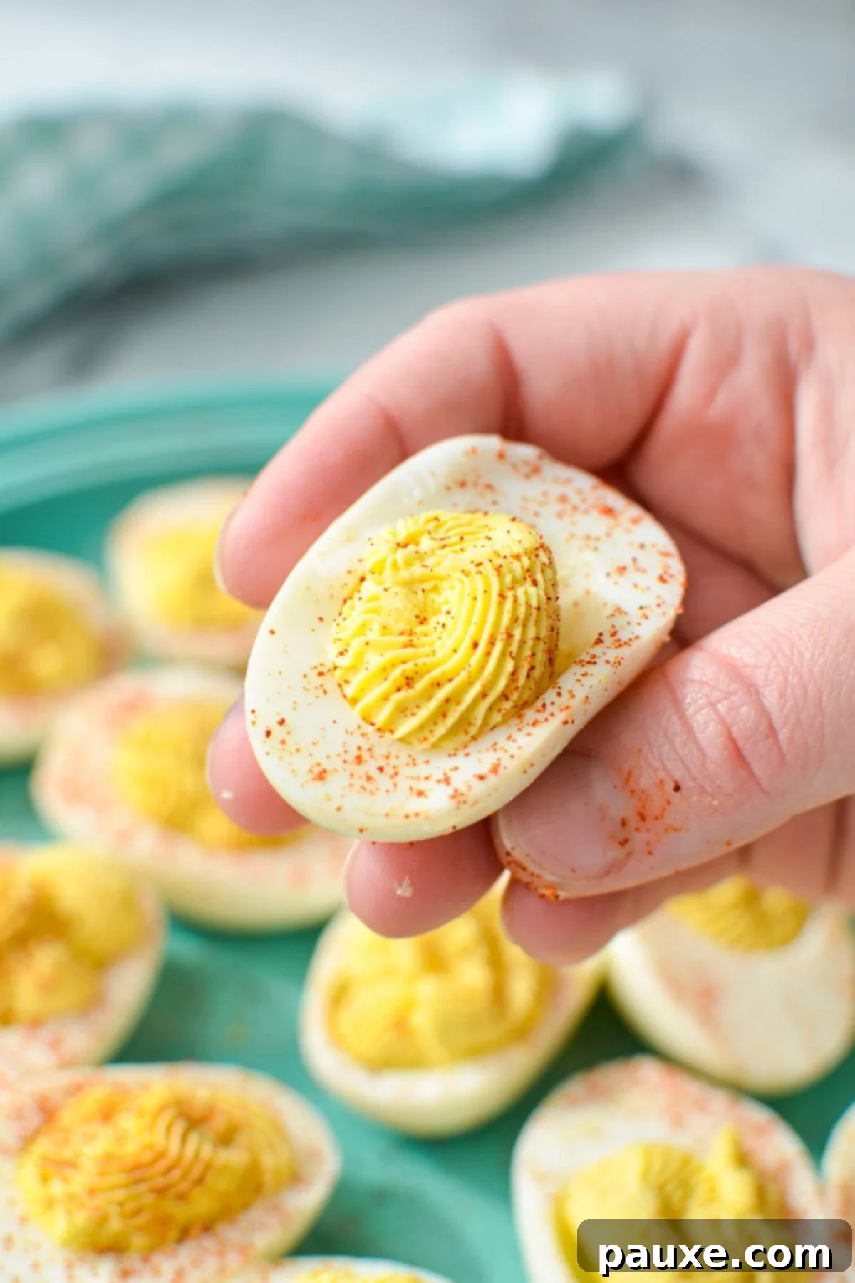 Effortless Instant Pot Deviled Eggs 9 A hand holding a deviled egg, sprinkled with paprika