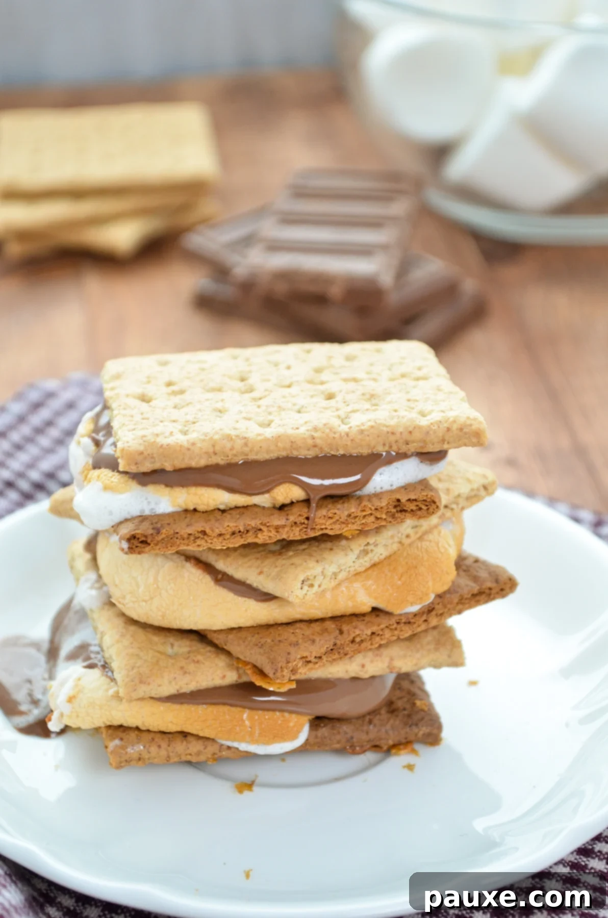 Air Fryer S'mores Magic 6 A stack of three s'mores with chocolate, marshmallows, and graham crackers in the background.
