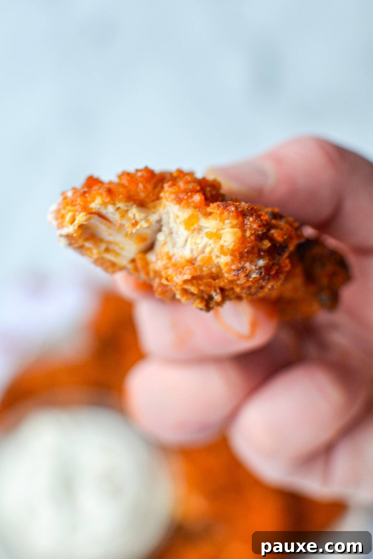 A close-up of a buffalo chicken tender with a bite taken out, showing the tender interior and crispy coating.