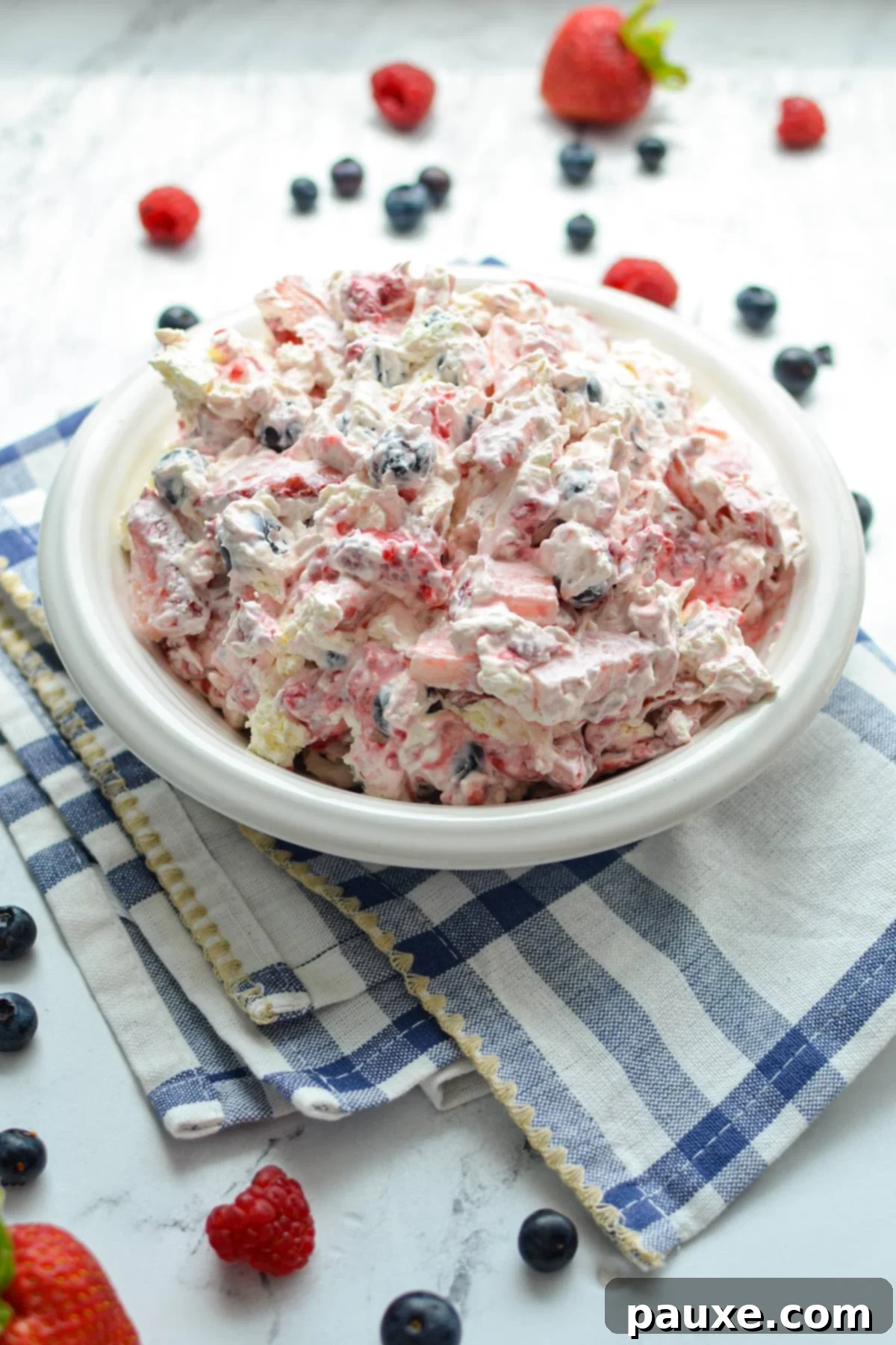 Red, White, and Blue Cheesecake Berry Bliss 7 A bowl of red white and blue cheesecake salad, in a bowl resting on top of a blue and white kitchen towel.