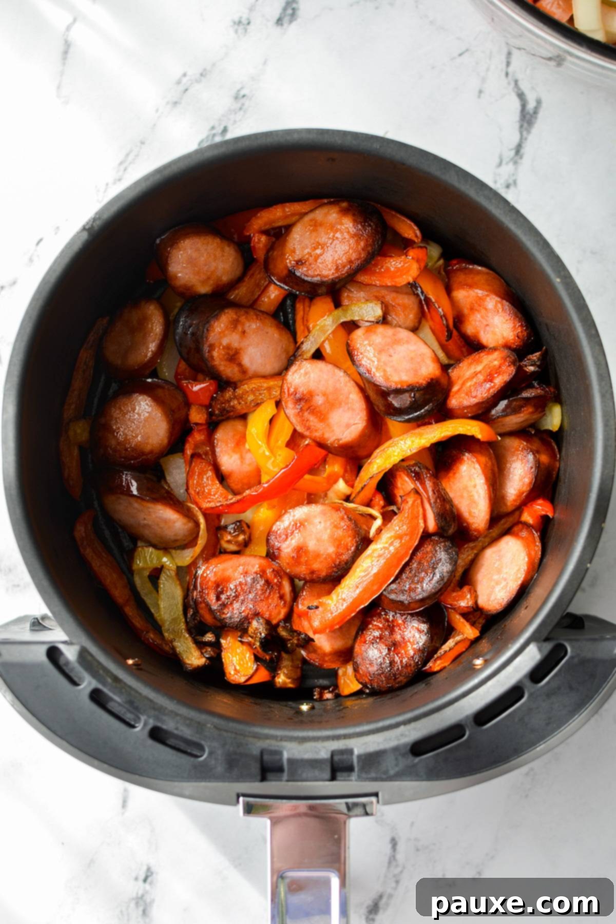 Crispy Air Fryer Sausage and Peppers 2 An overhead shot of an air fryer with cooked sausage and peppers.