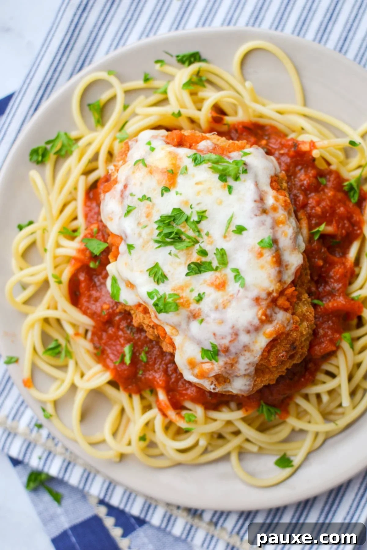 A vibrant plate of spaghetti noodles topped with golden-brown air-fried chicken parmesan, generously coated in rich marinara sauce and sprinkled with fresh parsley.
