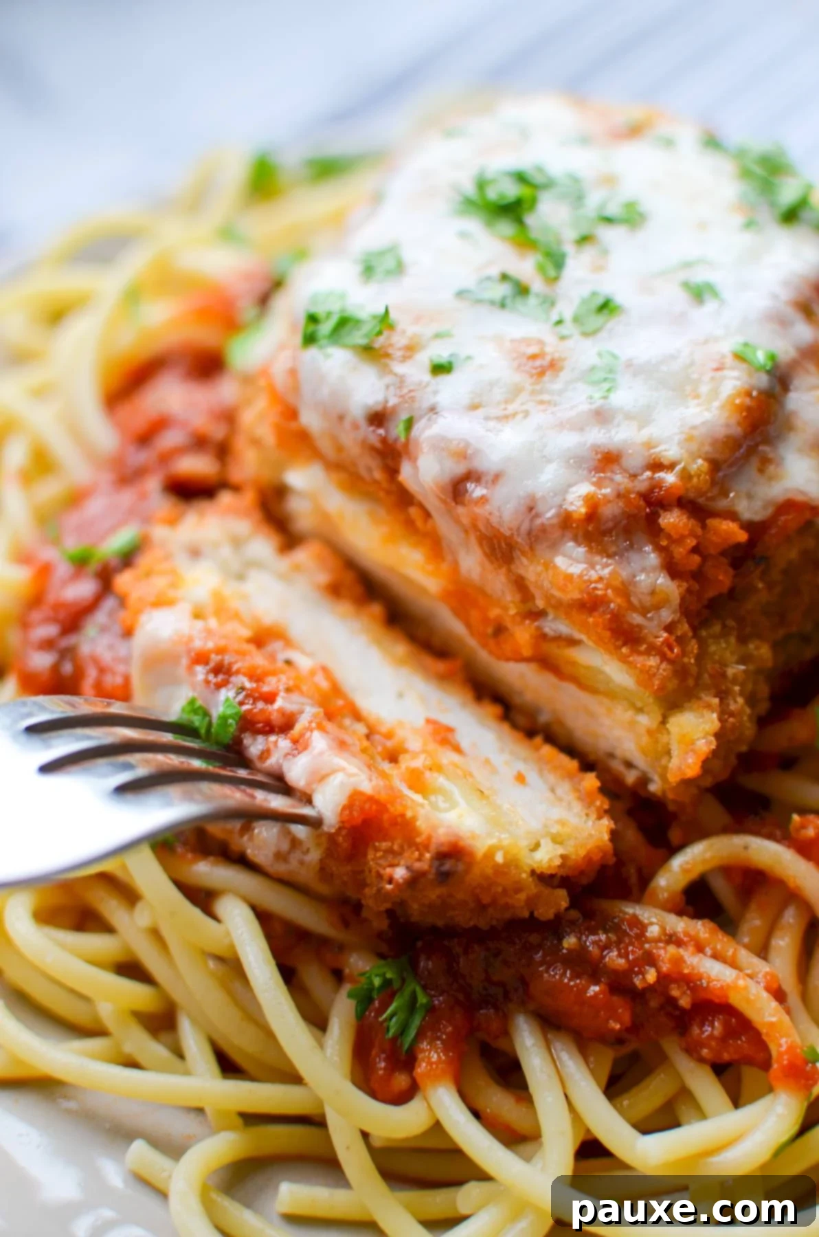 A fork piercing into a piece of air-fried chicken parmesan, showcasing its golden crust and tender interior.
