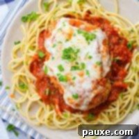 A plate of spaghetti topped with marinara sauce and a cutlet of chicken parmesan, garnished with fresh herbs.