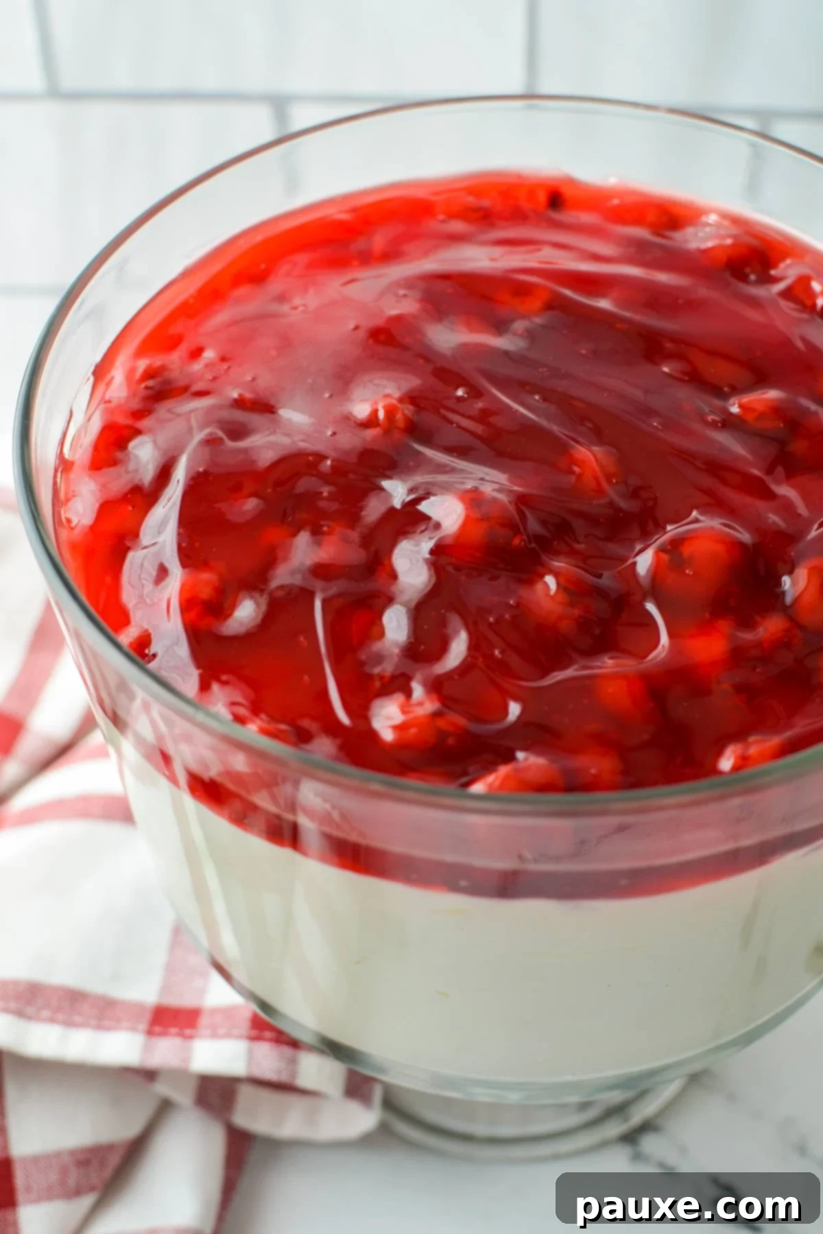 Effortless Cheesecake Delight 2 A beautiful trifle dish overflowing with layers of creamy lazy cheesecake salad and vibrant cherry pie filling, ready to be served.