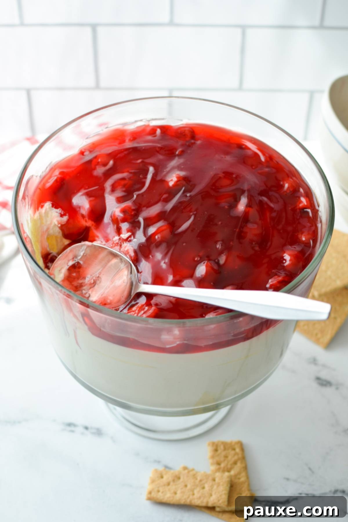 Effortless Cheesecake Delight 11 A wide, decorative trifle dish showcasing a thick, creamy layer of no-bake cheesecake base topped with a luscious fruit filling, ready for serving as a dessert dip.