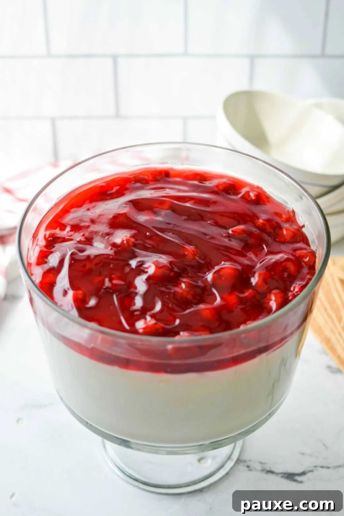 Effortless Cheesecake Delight 8 A beautifully layered trifle dish filled with creamy lazy cheesecake salad topped with glossy cherry pie filling, ready to be enjoyed.