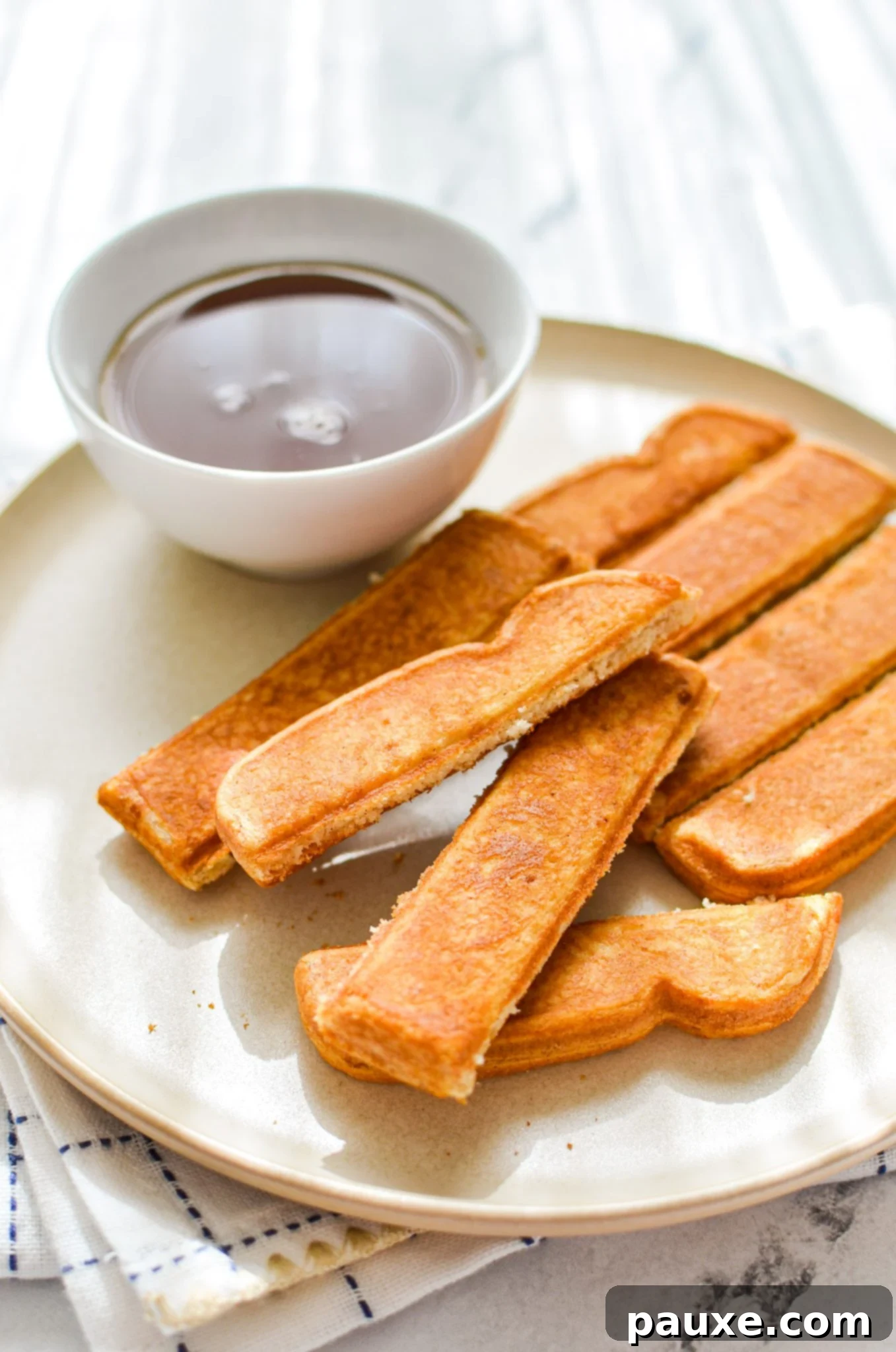 A beautifully plated breakfast featuring crispy air fryer frozen French toast sticks, accompanied by a small bowl of golden maple syrup, ready for dipping.