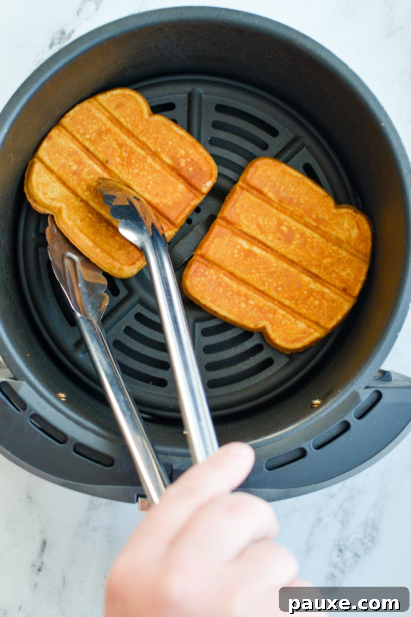 A hand gently flipping frozen French toast sticks over in the air fryer basket during cooking to ensure even browning and crispness.