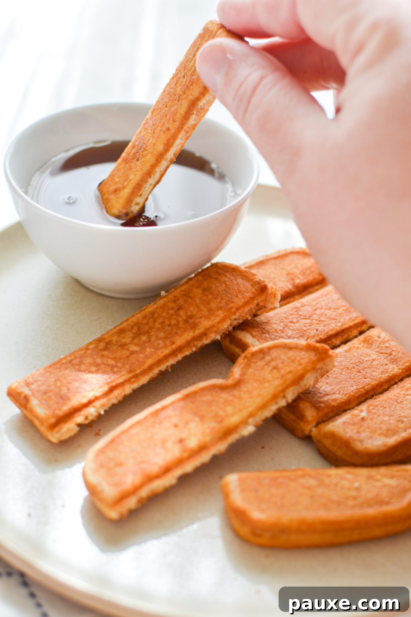 A single golden-brown French toast stick being dipped into a luscious pool of maple syrup, emphasizing its crispy texture.