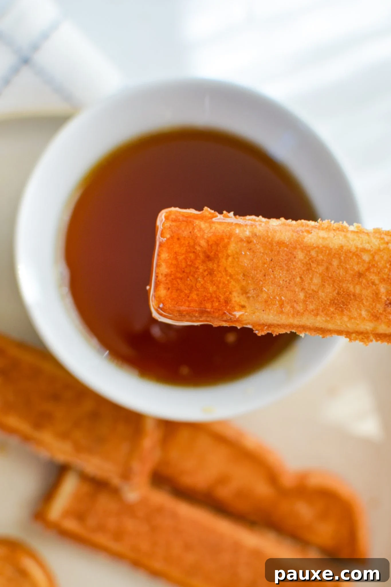 Two hands dipping crispy air fryer French toast sticks into a bowl of golden maple syrup, highlighting the delicious interaction.