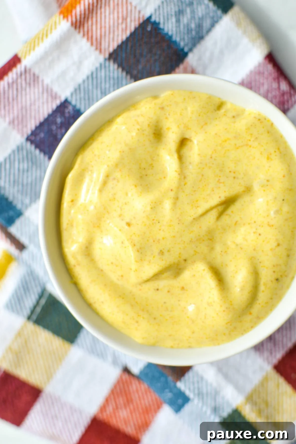 Creamy Homemade Curry Aioli 5 A small bowl of freshly made curry aioli resting on a checkered napkin, showcasing its creamy texture.