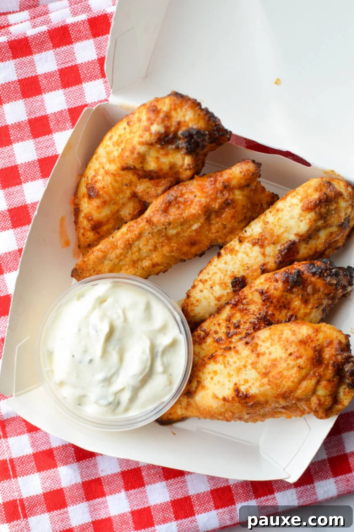 Air Fryer Naked Chicken Tenders 2 A small takeout box filled with golden-brown, unbreaded chicken tenders and a side of creamy ranch dip.