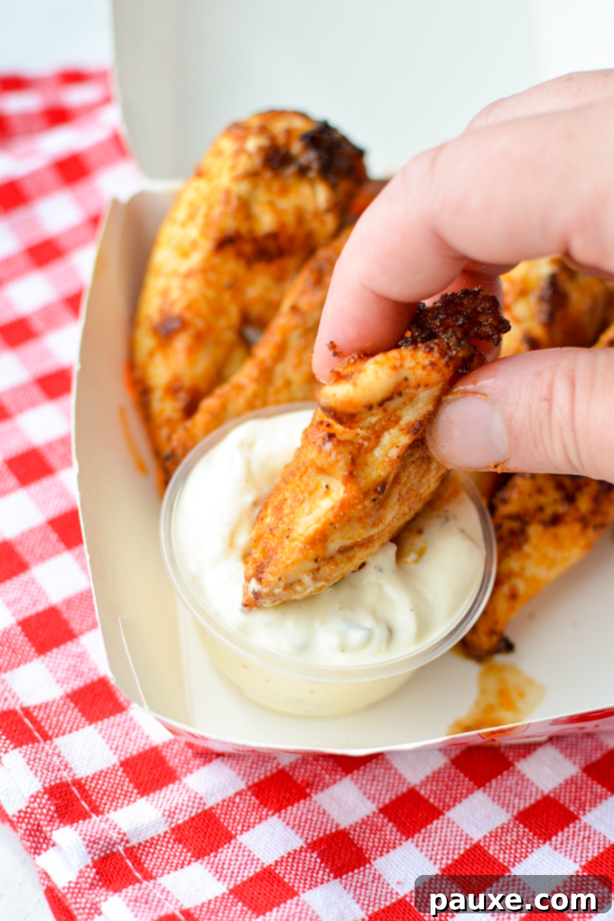 Air Fryer Naked Chicken Tenders 7 A perfectly cooked chicken tender being dipped into a bowl of creamy ranch dressing, highlighting its golden texture.