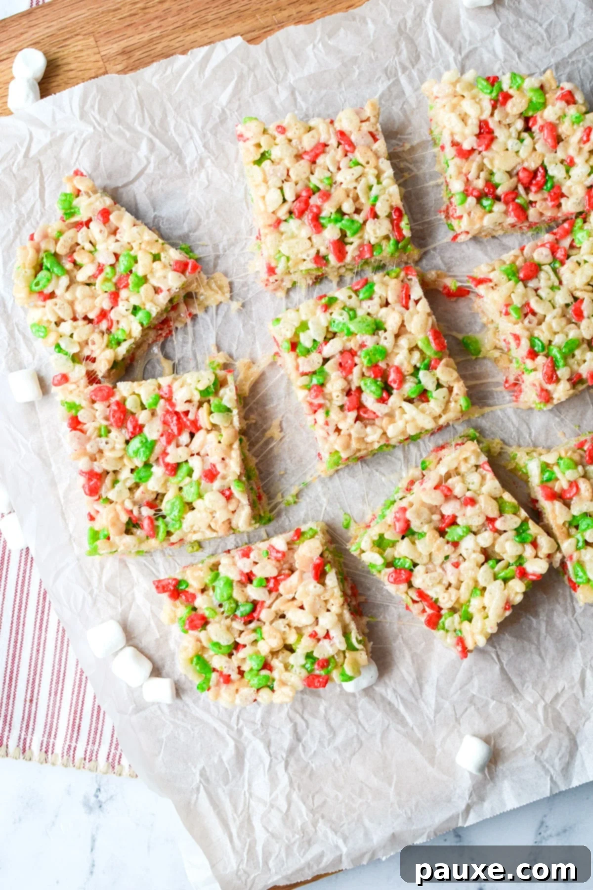Festive Christmas Rice Krispie Treats 8 9 cereal treats place on a piece of parchment on top of a cutting board.