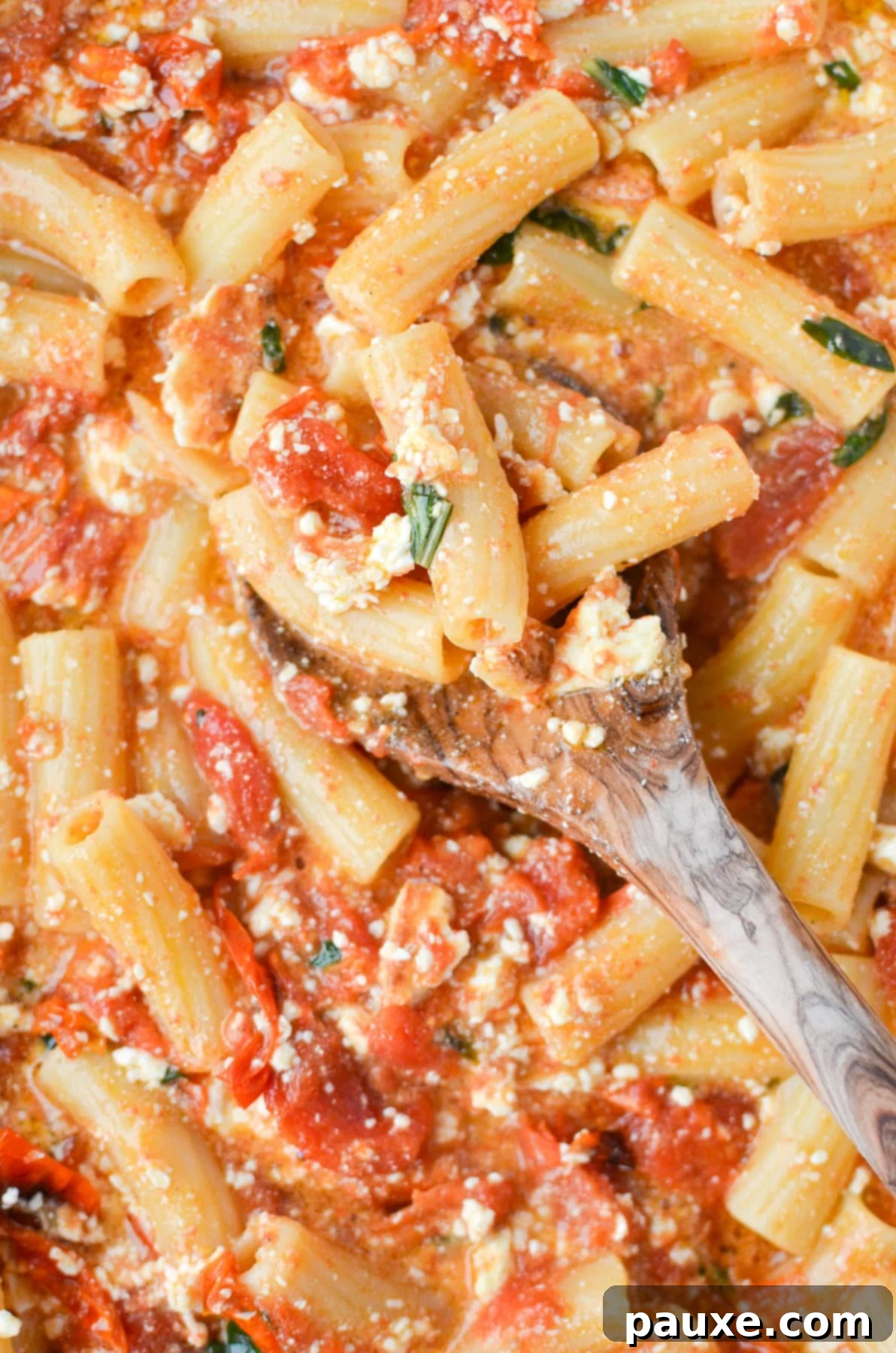 Roasted Tomato and Feta Pasta 8 A wooden spoon serving a portion of baked feta pasta from a baking dish, garnished with basil.