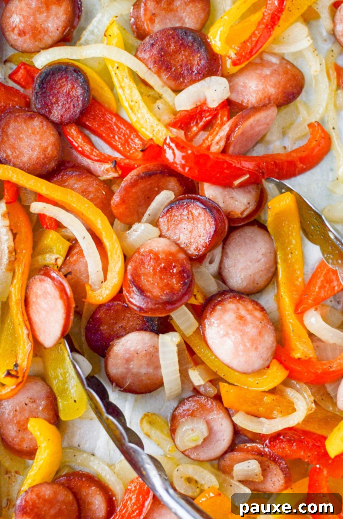One-Pan Smoked Sausage and Peppers Feast 7 A pair of kitchen tongs gracefully grabbing a serving of the savory smoked sausage, peppers, and onions from the sheet pan, highlighting its readiness.