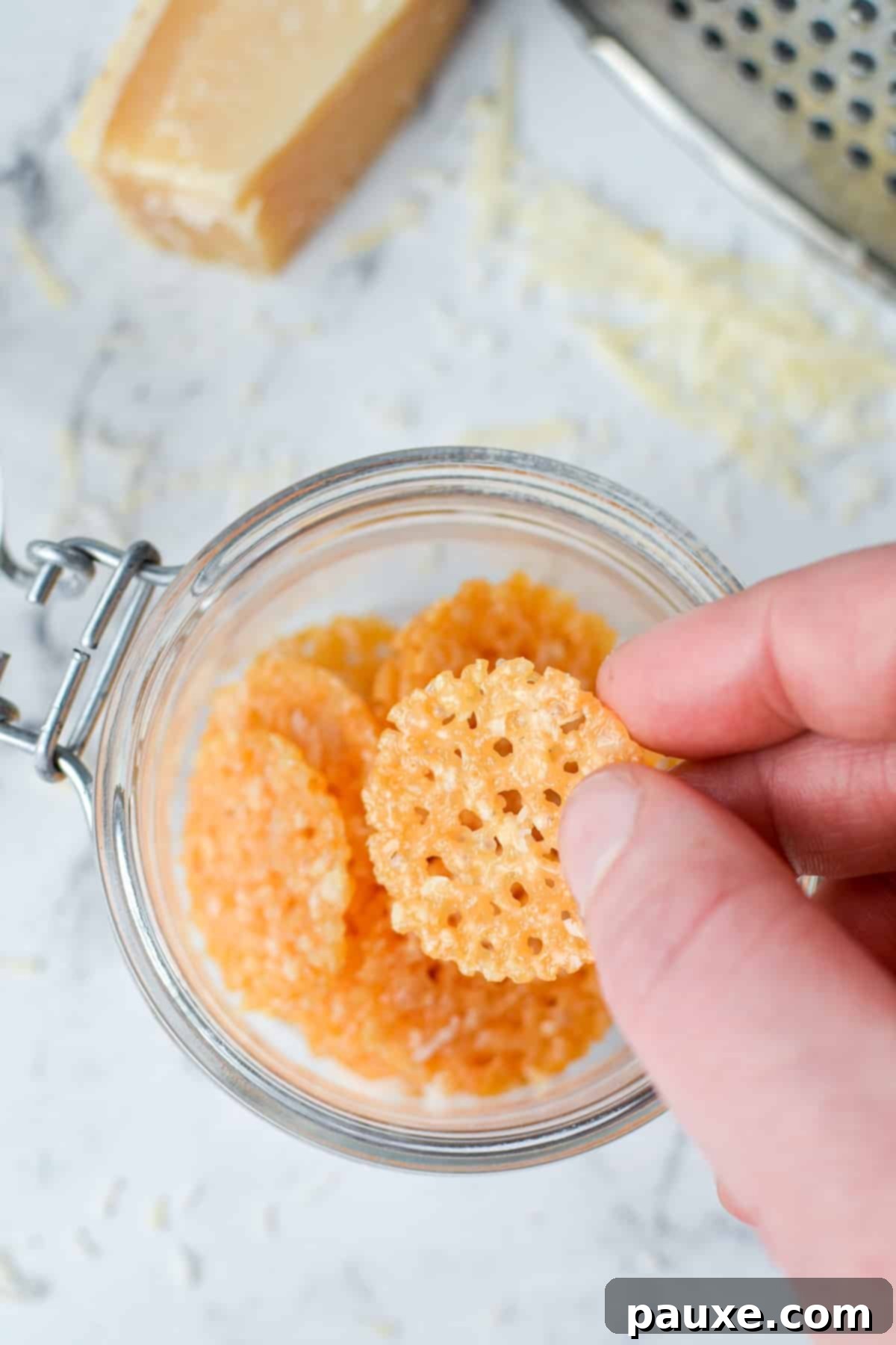 Crispy Parmesan Bites 10 A hand reaching into a glass jar to pick up a golden, crispy Parmesan chip, ready for a delicious bite.