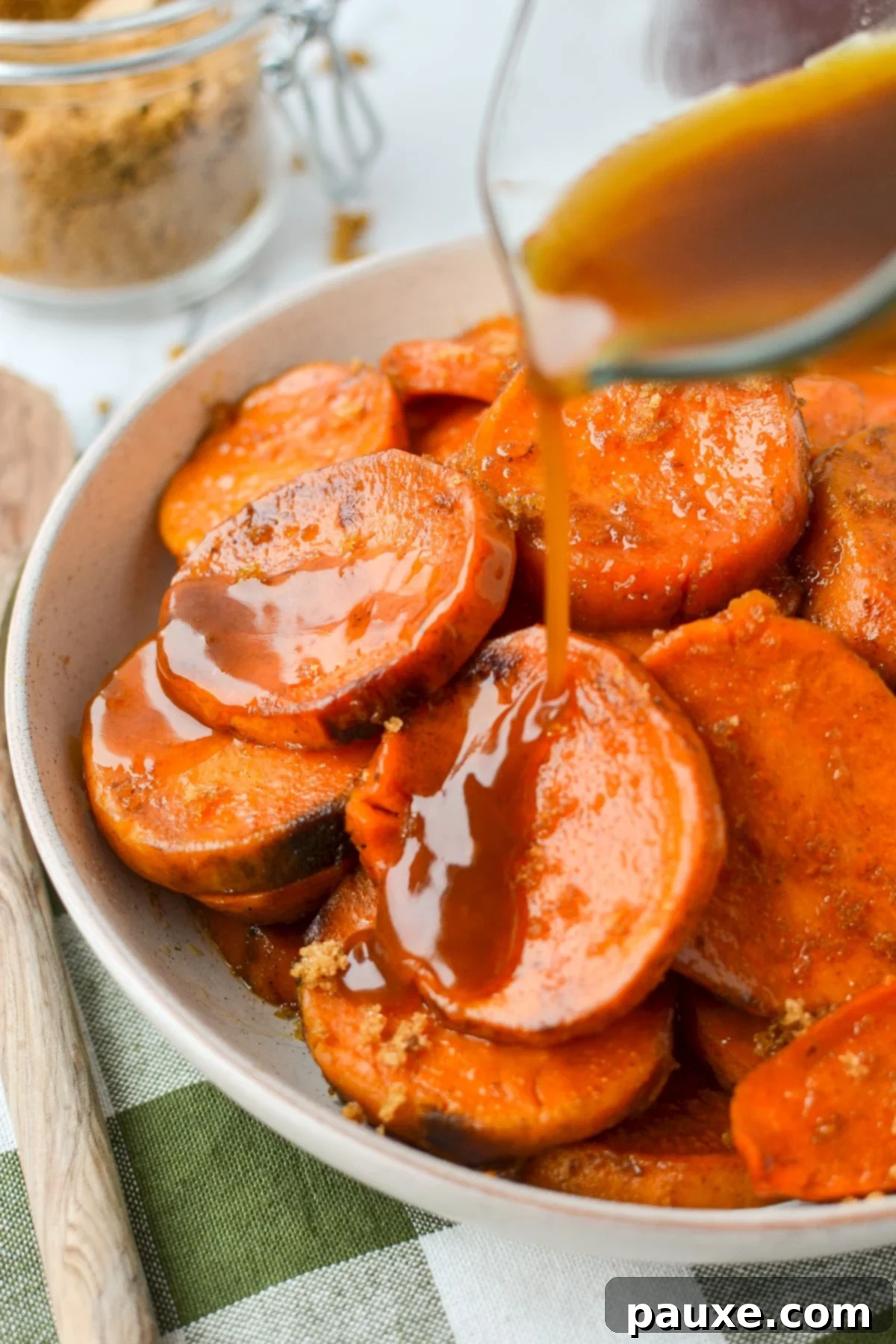 Slow Cooker Candied Sweet Potatoes 7 A stream of rich, thickened maple and brown sugar glaze being poured over a bowl of glistening, tender sweet potato rounds, enhancing their flavor and presentation for serving.