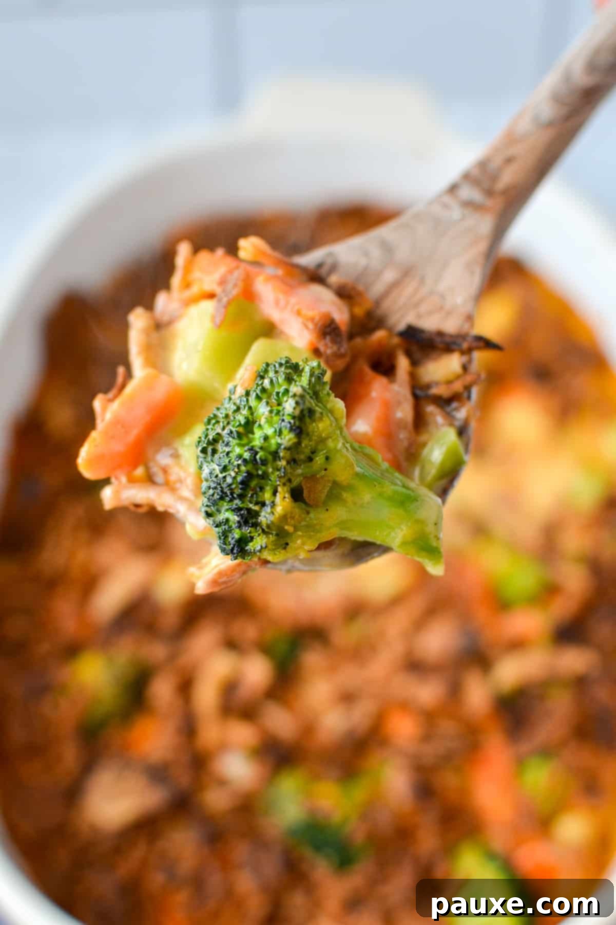 Golden Garden Gratin 8 A wooden spoon delicately scooping out a generous portion of cheesy vegetable casserole from a baking dish, revealing the rich, creamy texture and vibrant vegetables.