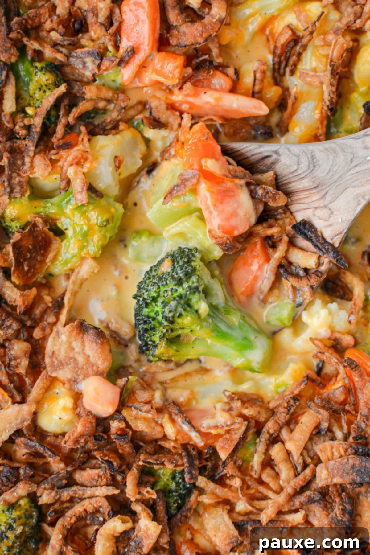 Golden Garden Gratin 9 A close-up of a serving of cheesy vegetable casserole with broccoli, scooped onto a plate with a wooden spoon, showcasing the creamy texture and melted cheese.