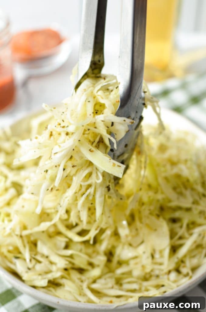 Swedish Pizza Slaw 9 Tongs taking a generous portion of a zesty coleslaw, made with a light vinegar-based dressing, from a serving bowl.