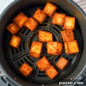 An air fryer basket with paneer cubes in it, illustrating the final dish.