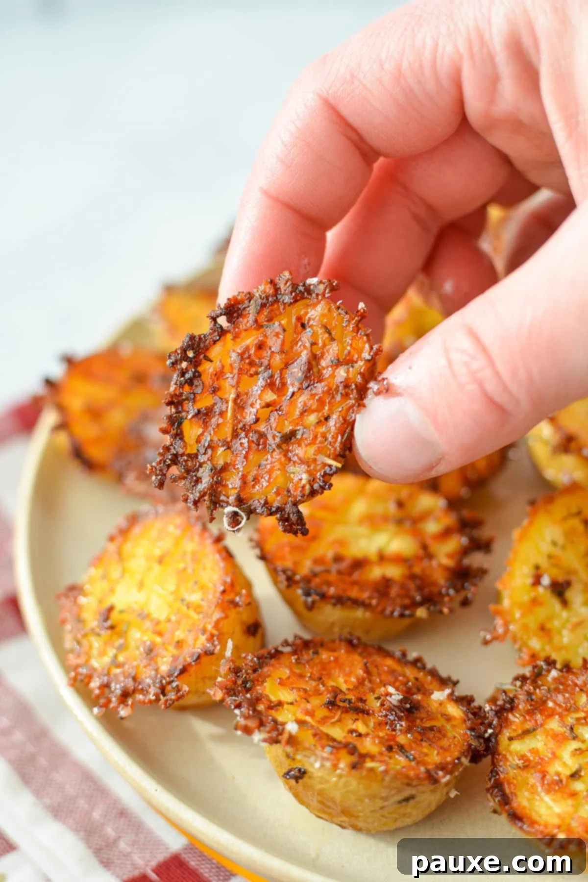 Crispy Garlic Parmesan Potatoes 9 A hand taking a small potato from a plate of roasted parmesan potatoes.