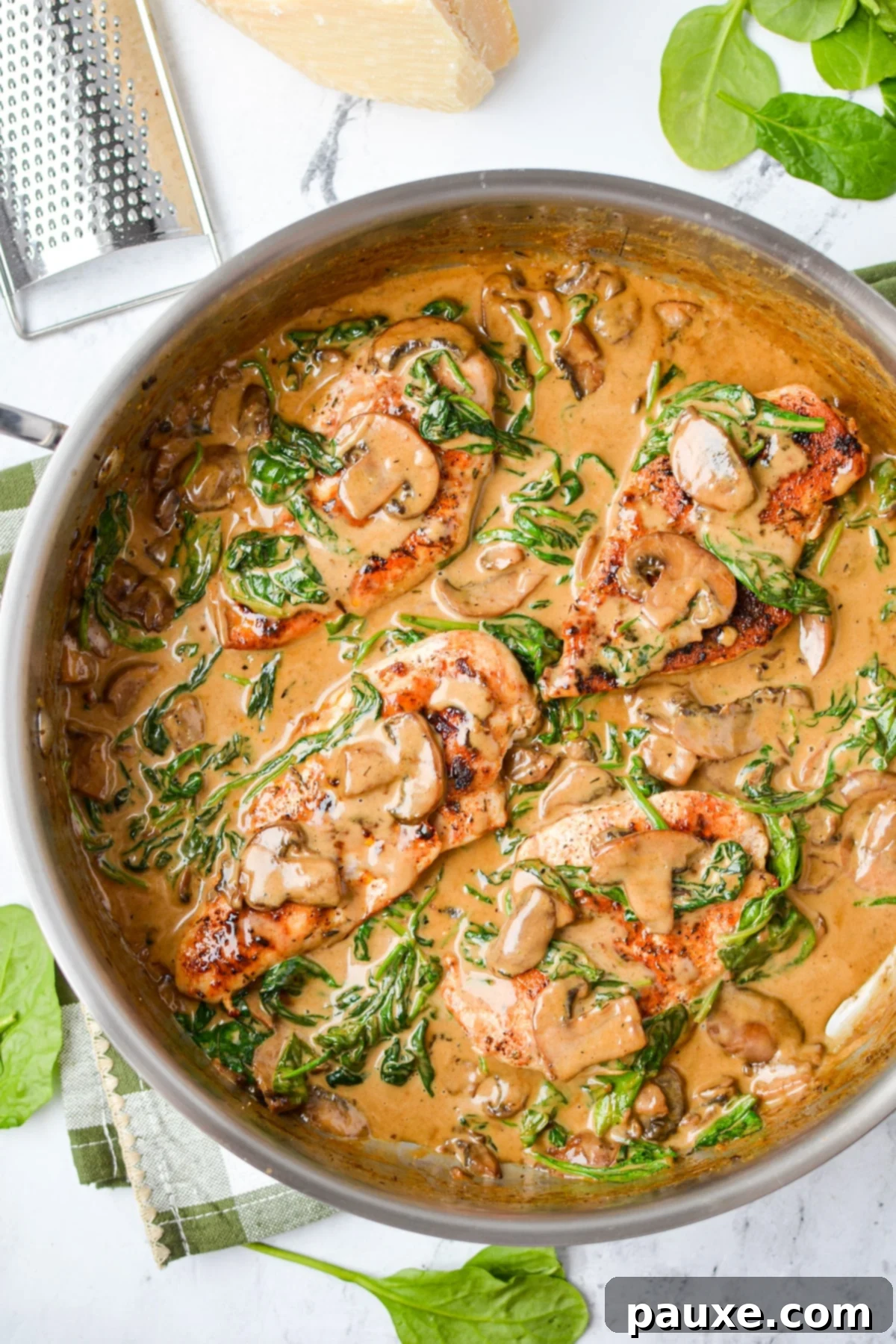 Creamy Mushroom and Spinach Chicken Delight 9 A gourmet presentation of creamy chicken with spinach and mushrooms in a skillet, garnished with fresh herbs and a wedge of Parmesan cheese.